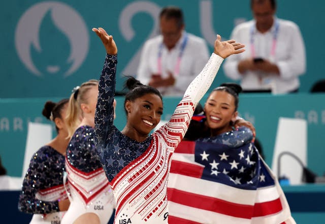 <p>Simone Biles saluda a la afición estadounidense mientras sus compañeras celebran</p>