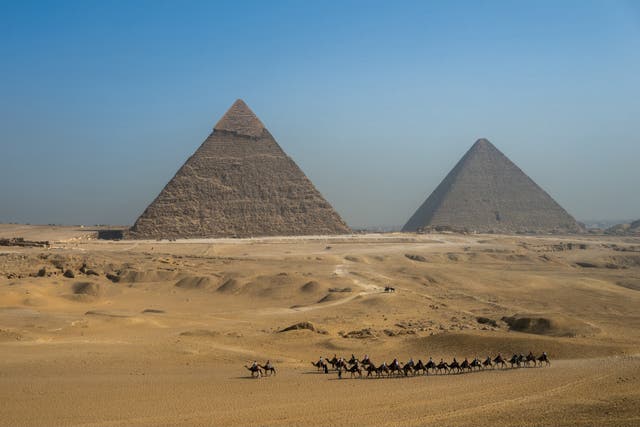 <p>Turistas pasean en camello junto a la Gran Pirámide de Khufu (dcha.) y la Pirámide de Khafre (izq.) en la Necrópolis de las Pirámides de Giza</p>