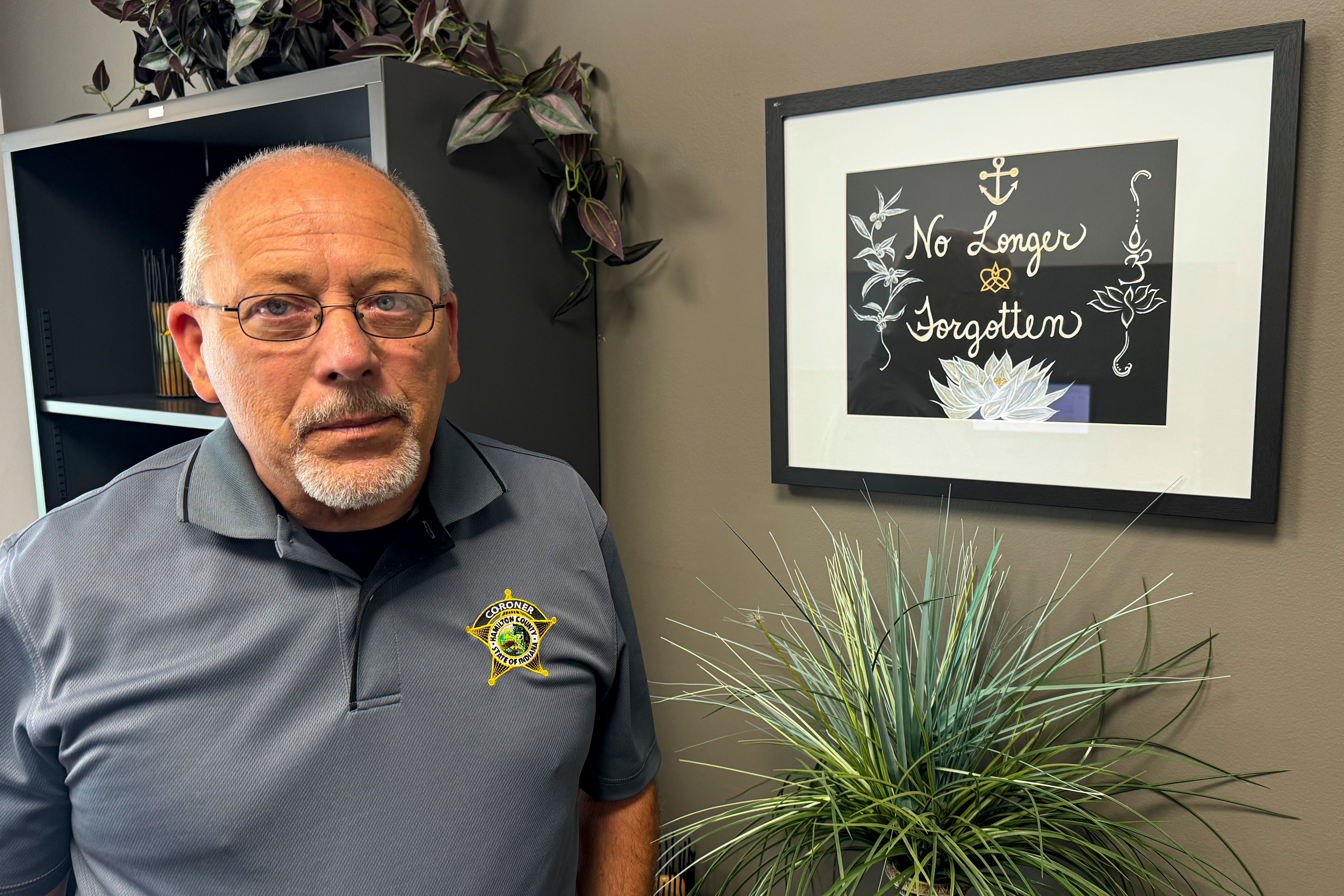 Jeff Jellison, forense del condado de Hamilton, se encuentra en su oficina el 11 de julio de 2024, frente a un cuadro en el que se lee ‘No Longer Forgotten’ (Dejó de ser un recuerdo) que su esposa creó como recordatorio de su trabajo en curso para identificar unos 10.000 huesos humanos y fragmentos de huesos desenterrados en la propiedad de Baumeister en los suburbios de Indianápolis a partir de 1996