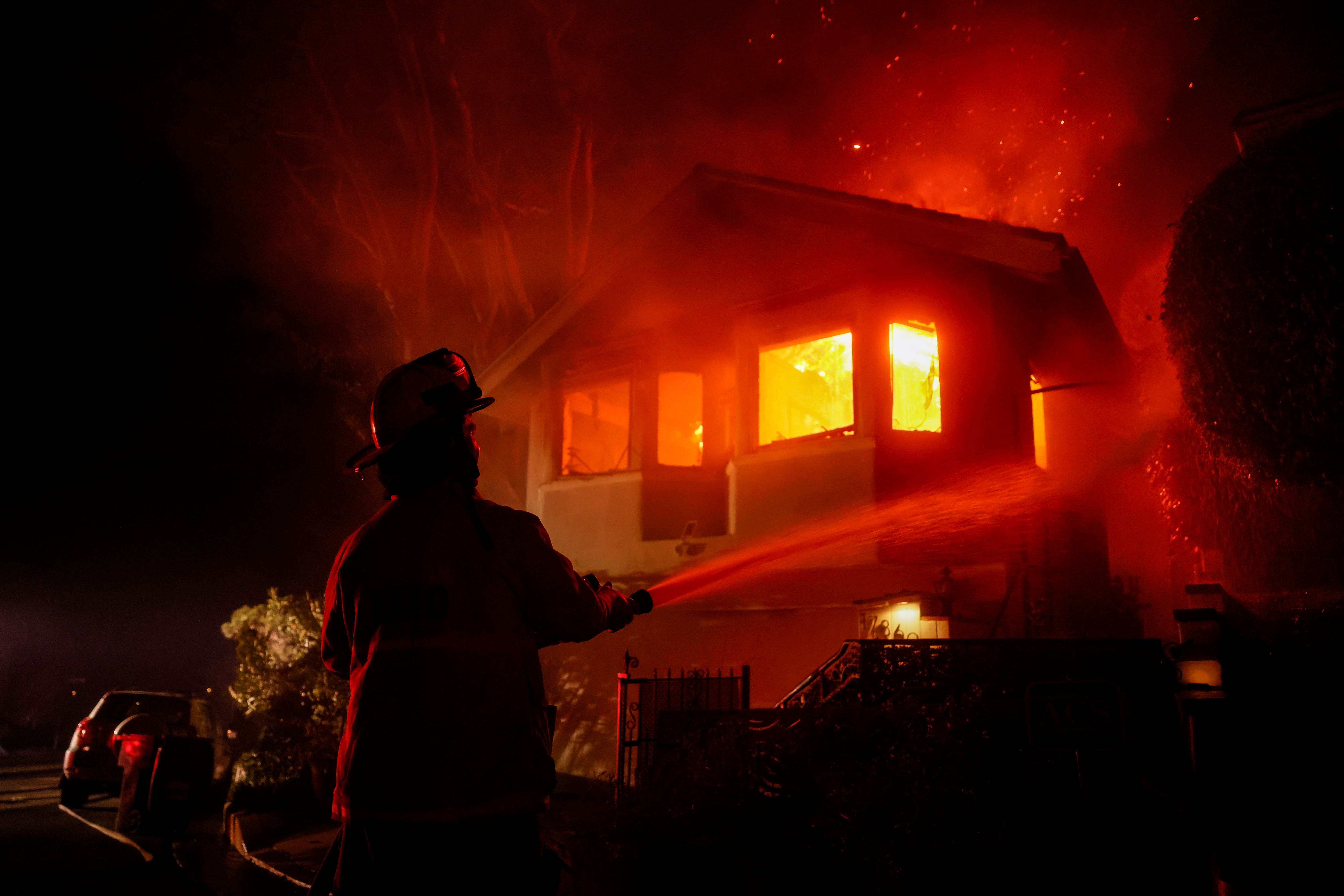 La foto de un bombero, mientras un incendio en Palisades quema una casa en la colina junto a la Villa Getty (AP Photo/Etienne Laurent)