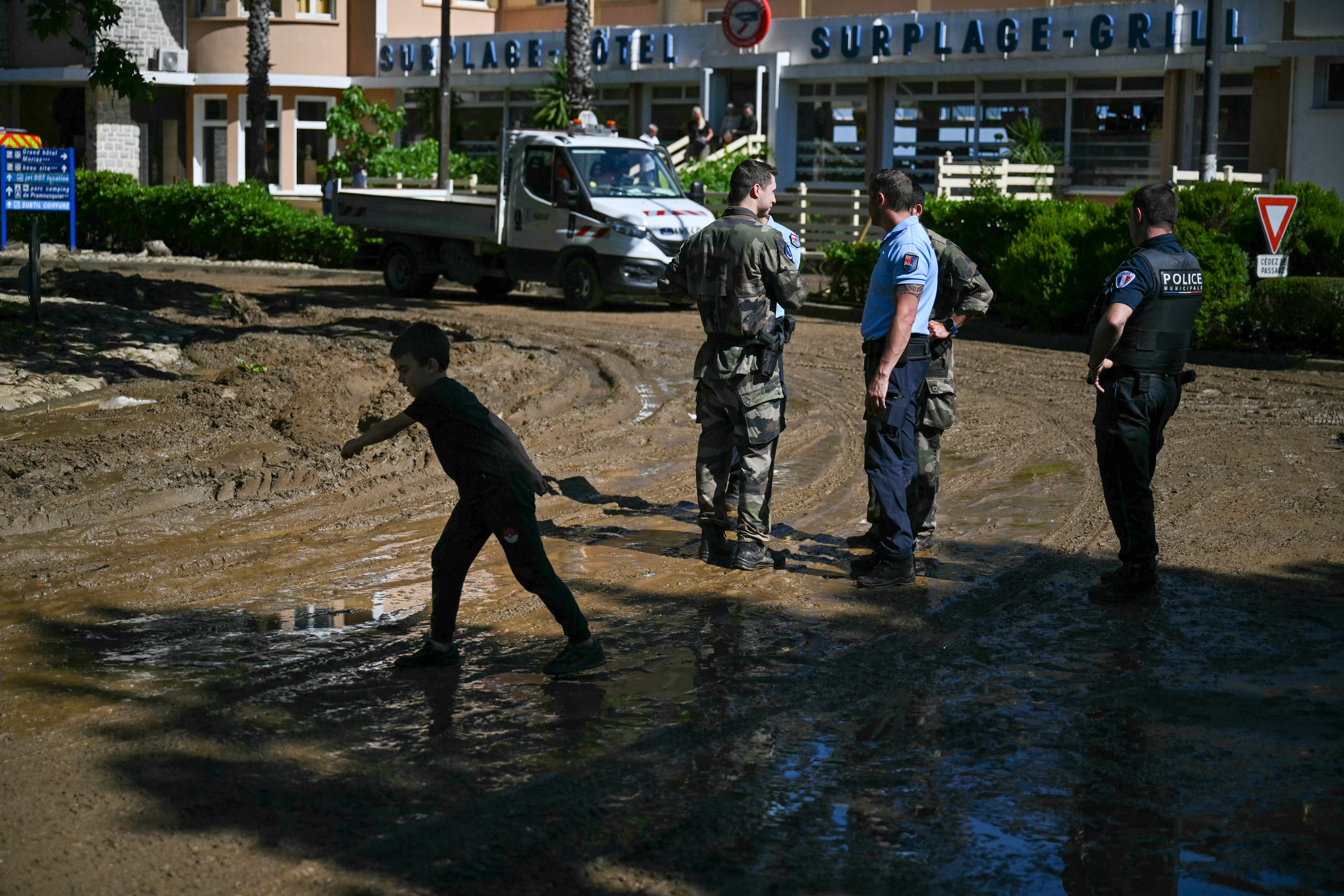 Un niño pasa junto a policías franceses en una calle cubierta de lodo tras una inundación provocada por las fuertes lluvias en el pueblo de Cavaliere