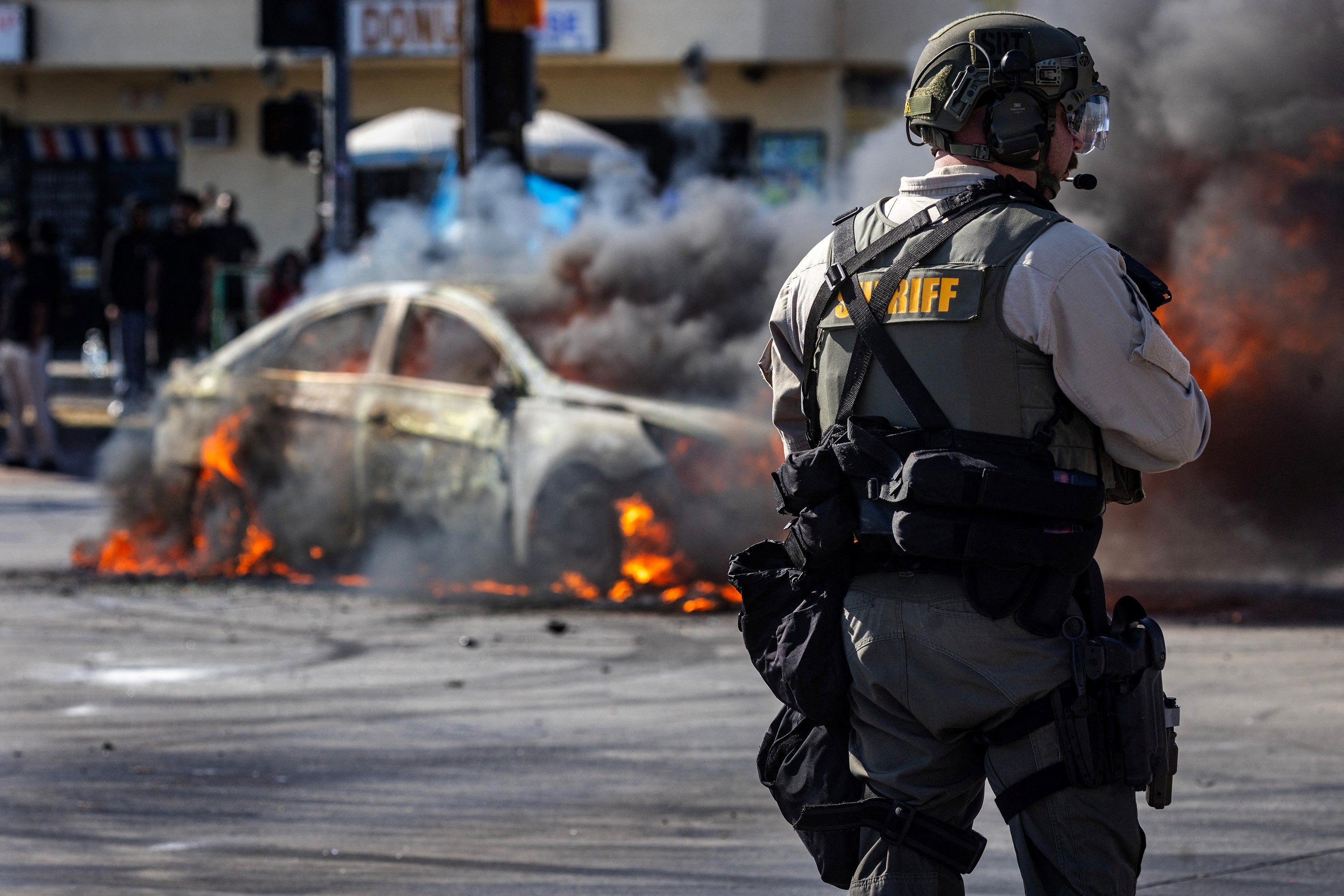 El humo sale de un coche incendiado sobre Atlantic Boulevard durante un enfrentamiento entre manifestantes y policías, tras varias detenciones por parte de ICE, en Paramount