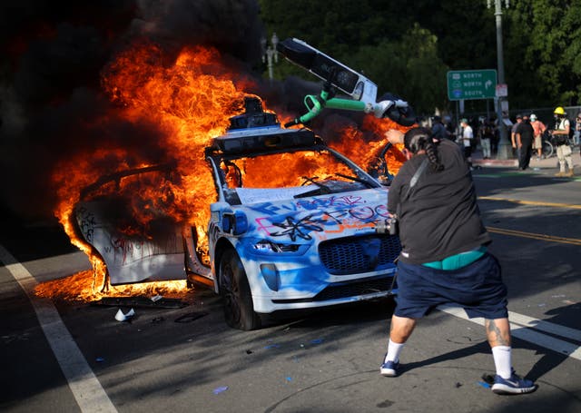 <p>Un manifestante lanza un patinete eléctrico contra un coche en llamas durante una protesta contra las redadas federales de inmigración en el centro de Los Ángeles</p>