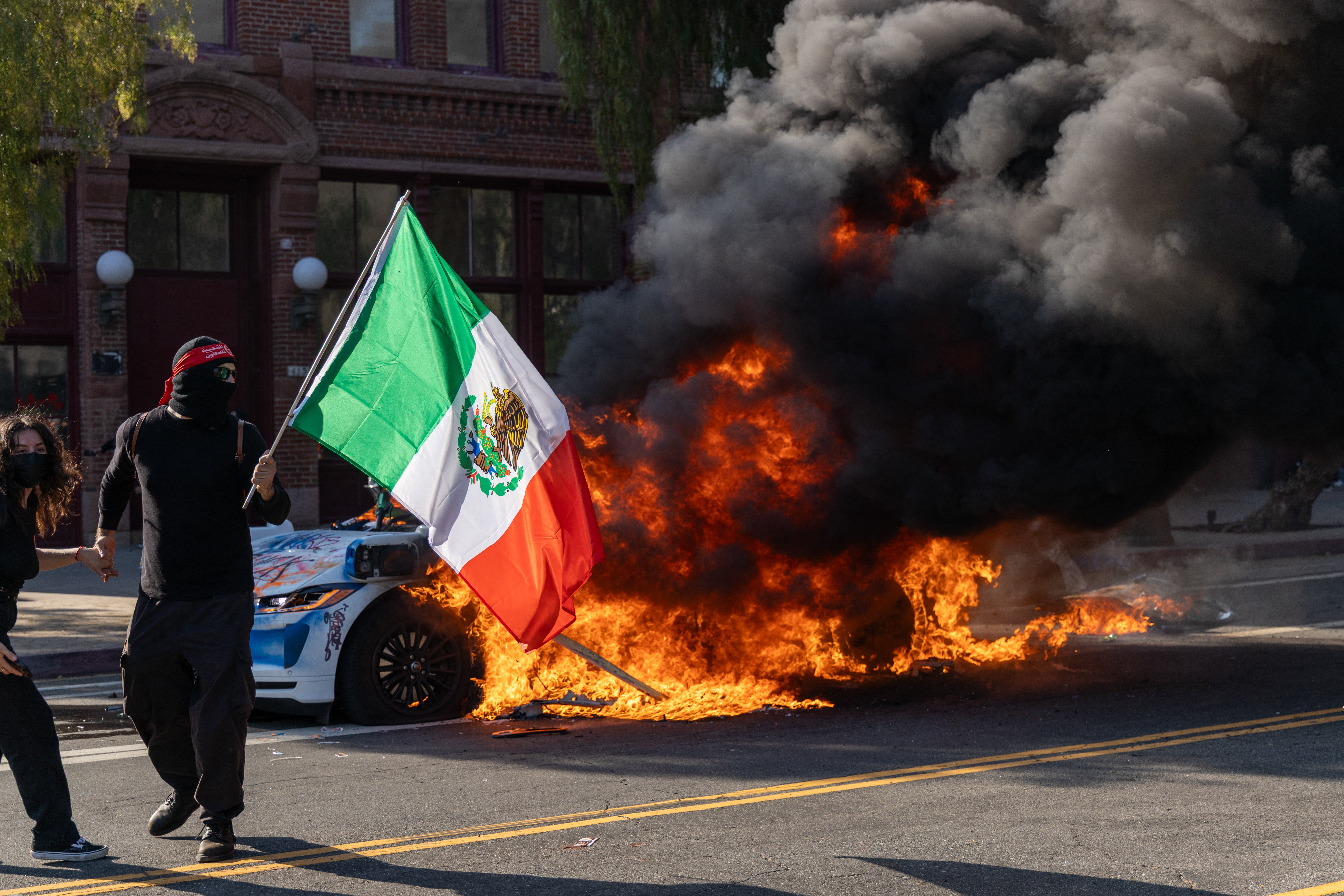 Un manifestante ondea una bandera mexicana frente a un vehículo en llamas durante una protesta en Los Ángeles