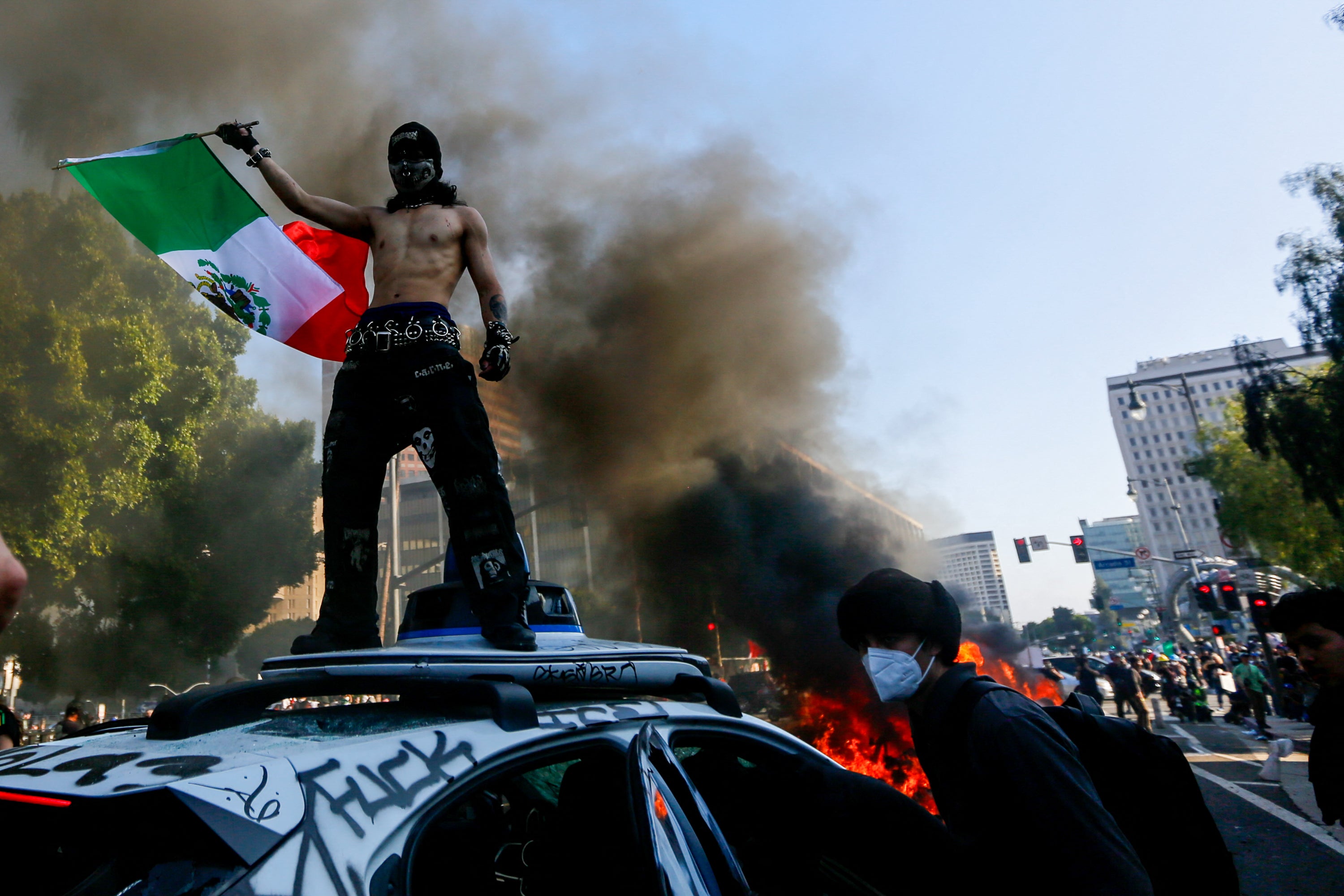 Un manifestante ondea la bandera mexicana encima de un vehículo autónomo durante una protesta anti-ICE en el centro de Los Ángeles