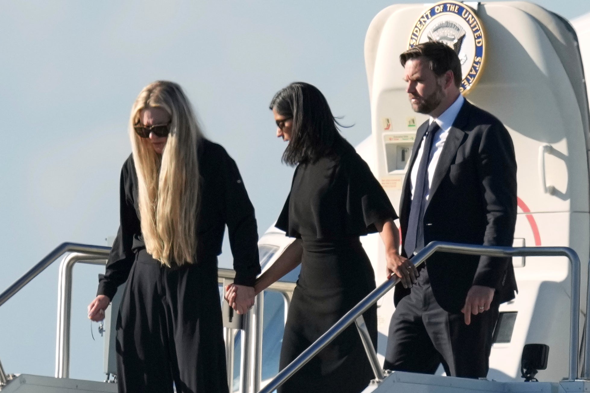 El vicepresidente J. D, Vance (a la derecha), la segunda dama Usha Vance (al centro) y Erika Kirk, quien lleva una cruz colgada en una cadena, descienden del Air Force Two, que traslada el cuerpo de Charlie Kirk