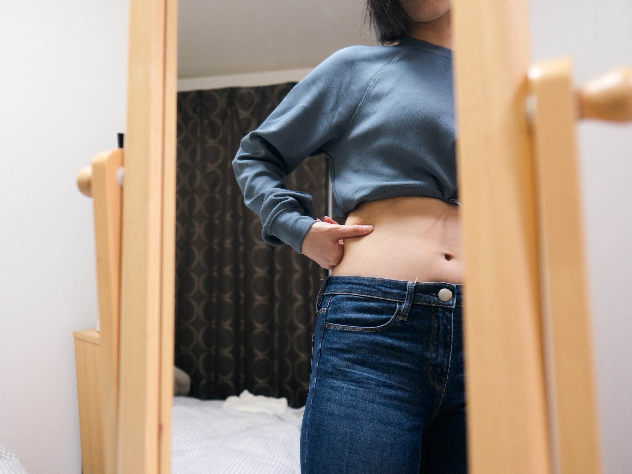 Joven mirando su abdomen frente al espejo