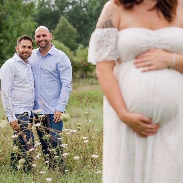 Ariel Taylor posa para una sesión de fotos durante uno de sus embarazos como gestante subrogada, con los futuros padres al fondo