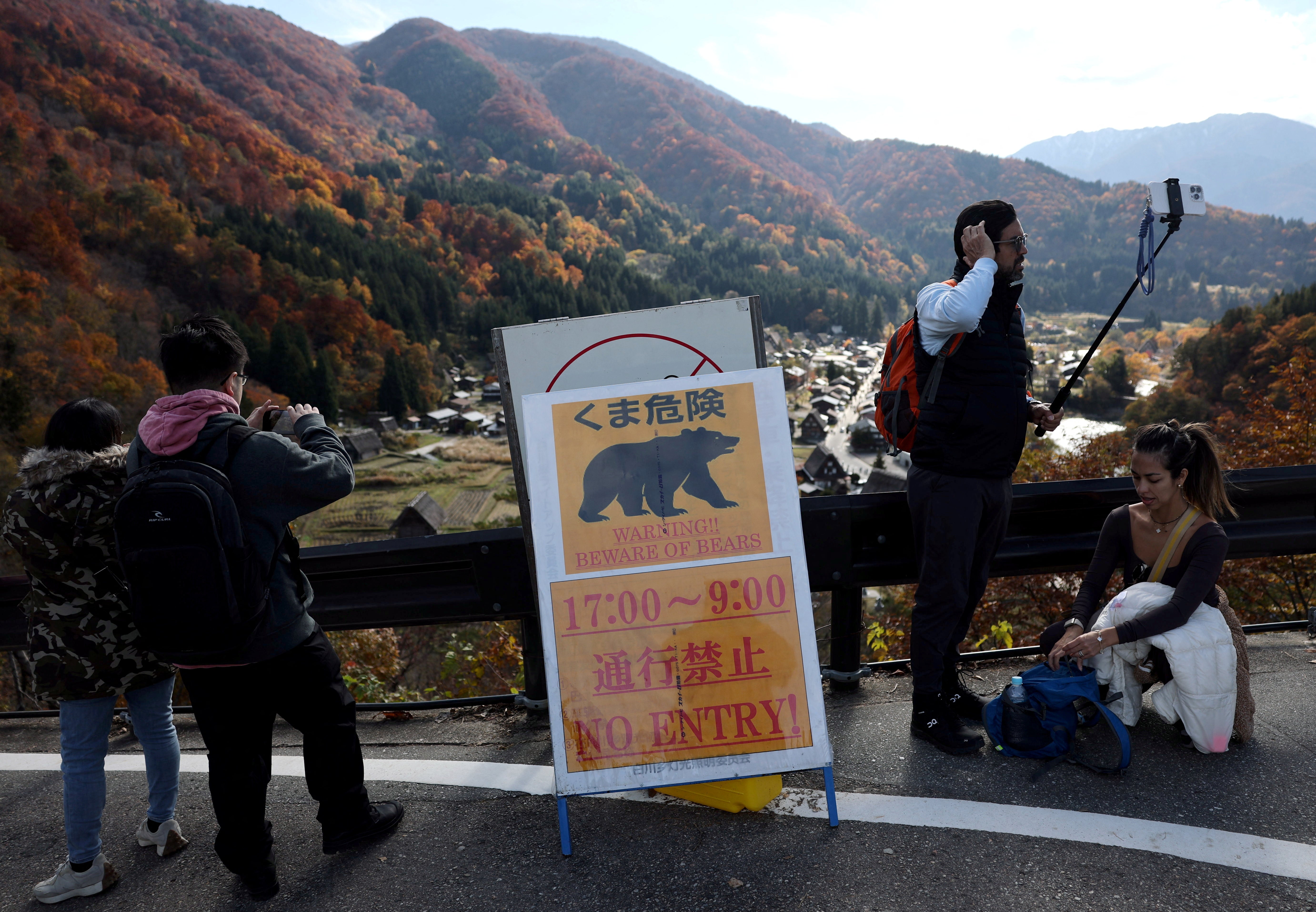 Turistas toman fotos cerca de un cartel que advierte sobre osos en la aldea de Shirakawa, prefectura de Gifu, Japón