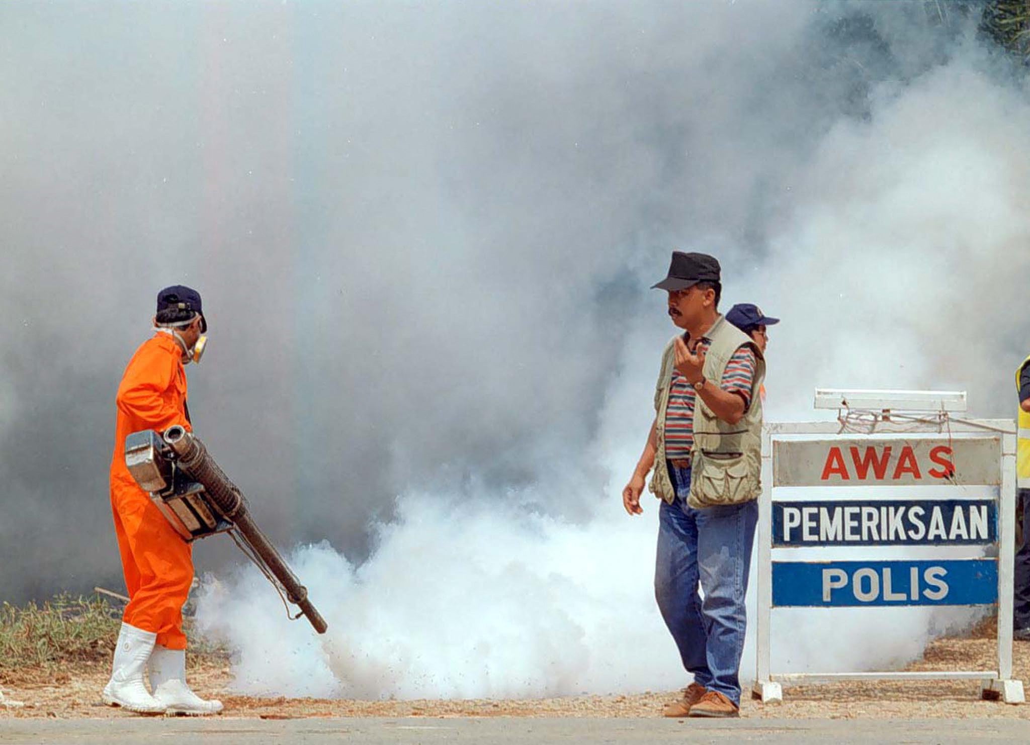 Archivo Un funcionario dirige el tránsito mientras otro fumiga la zona de Seelong, en el estado sureño de Johor, el 10 de mayo de 1999. Malasia amplió su operación de sacrificio de cerdos a Johor y al estado oriental de Kelantan después de que pruebas detectaran resultados positivos del letal virus Nipah en 40 animales