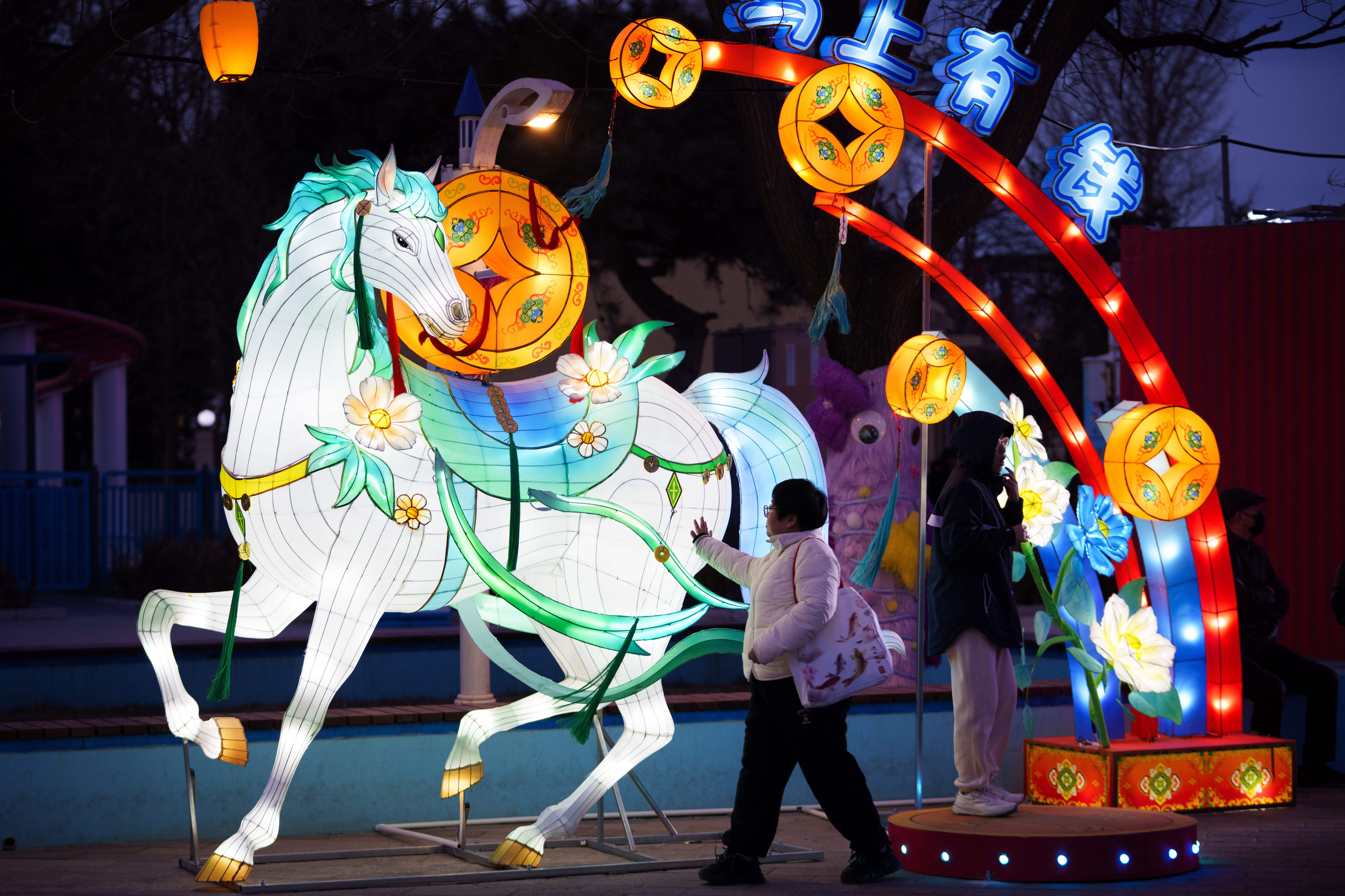 <p>Unos visitantes pasan junto a una exhibición de linternas de caballos iluminadas antes de las celebraciones del Año Nuevo lunar en un parque de atracciones a las afueras de Pekín, China</p>