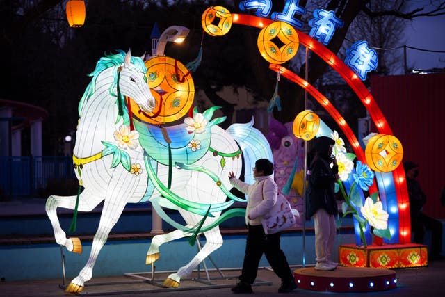 <p>Unos visitantes pasan junto a una exhibición de linternas de caballos iluminadas antes de las celebraciones del Año Nuevo lunar en un parque de atracciones a las afueras de Pekín, China</p>