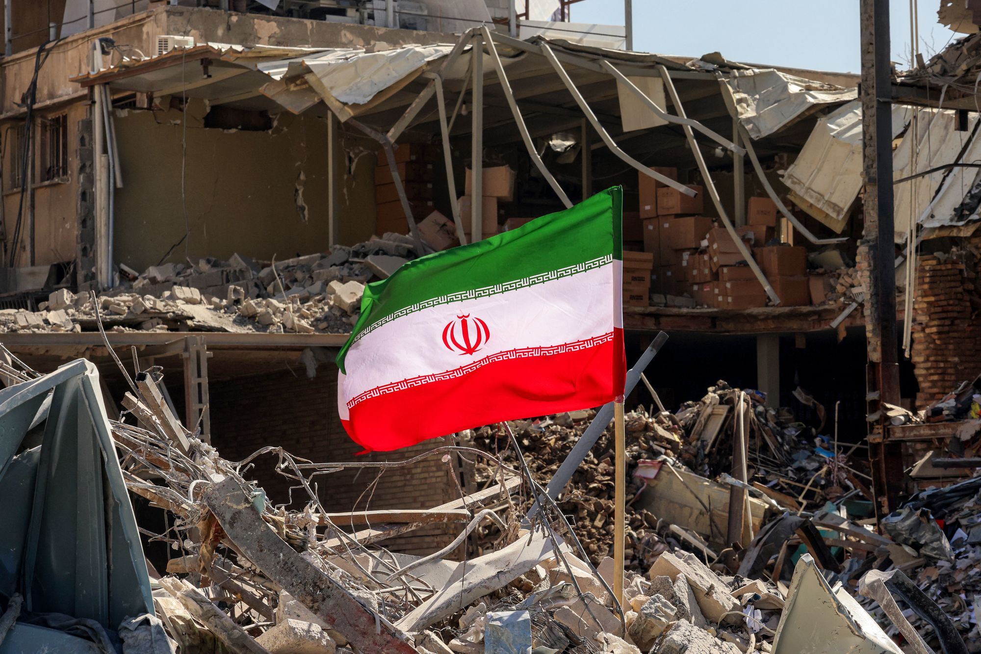 Una bandera iraní permanece en pie entre los escombros de un edificio residencial destruido cerca de la plaza Ferdowsi, en Teherán