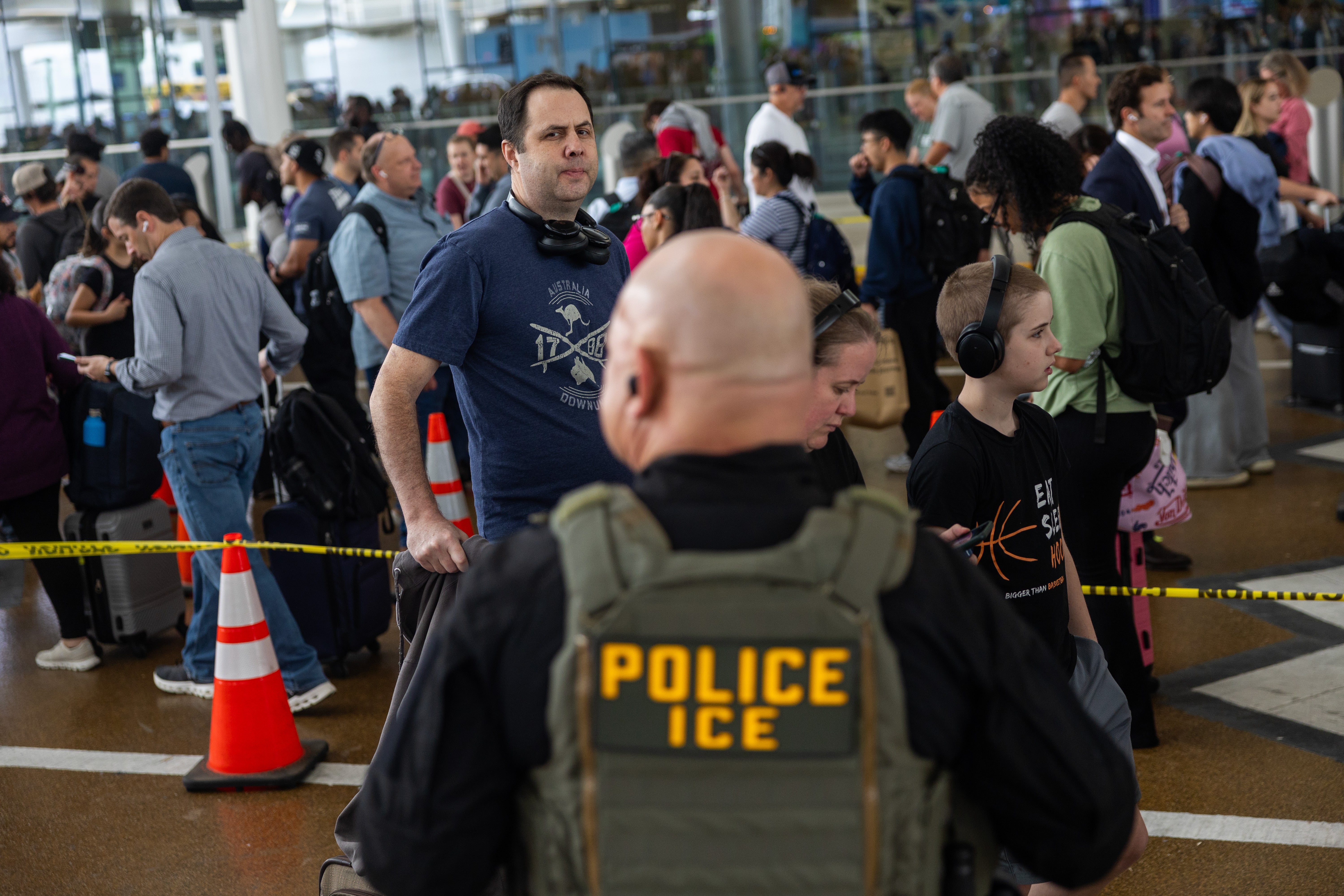 <p>Unos viajeros esperan en fila en el Aeropuerto Intercontinental George Bush de Houston bajo la mirada de un agente del ICE, el 24 de marzo de 2026, en medio de un cierre parcial del Gobierno que está provocando escenas similares en todo el país</p>