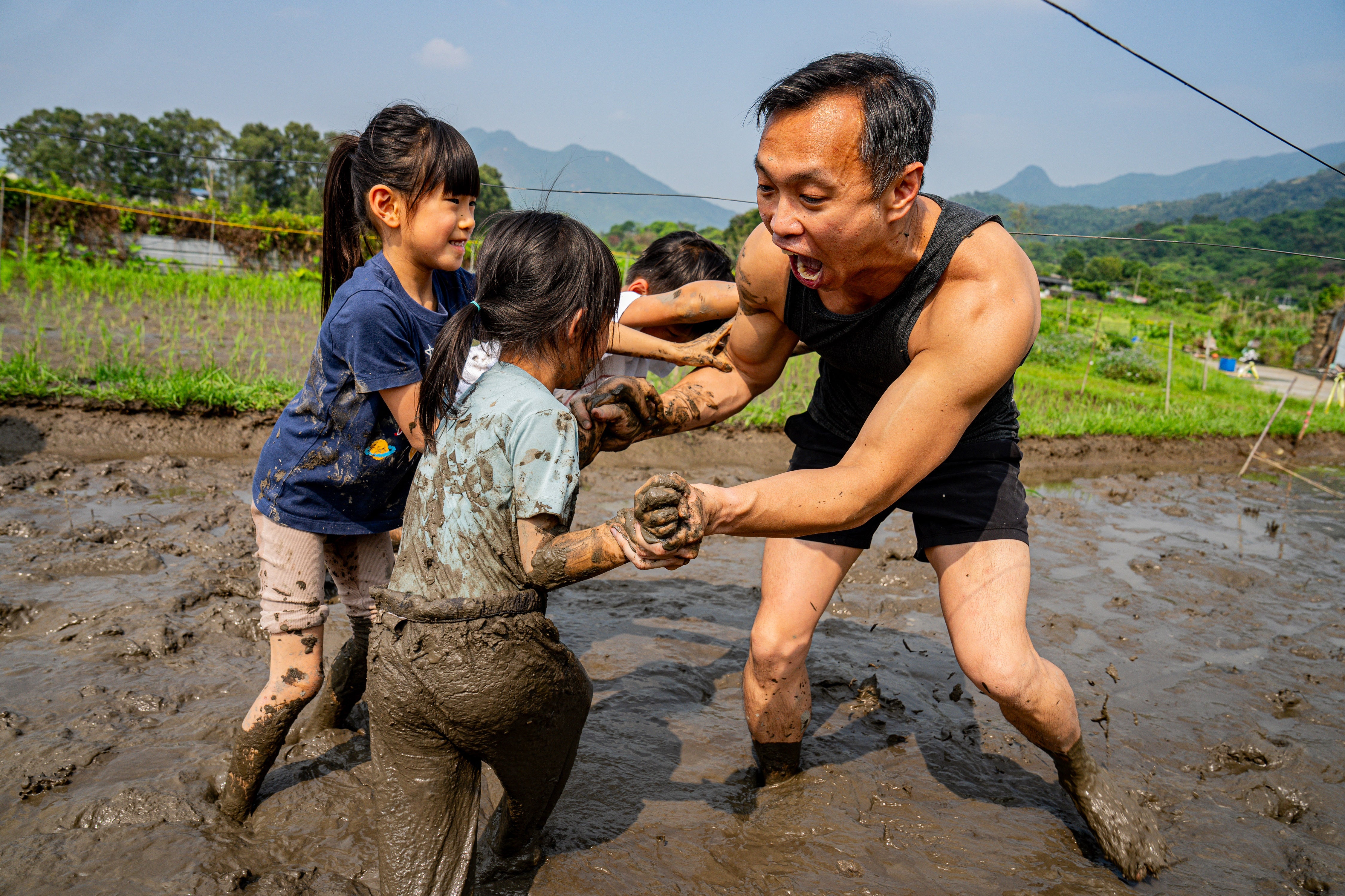 Un hombre se une a unos niños en una actividad de lucha en el barro en un campo embarrado durante un evento organizado, que incluye carreras en el barro y combates de lucha, celebrado en Hong Kong, China, el 18 de abril de 2026