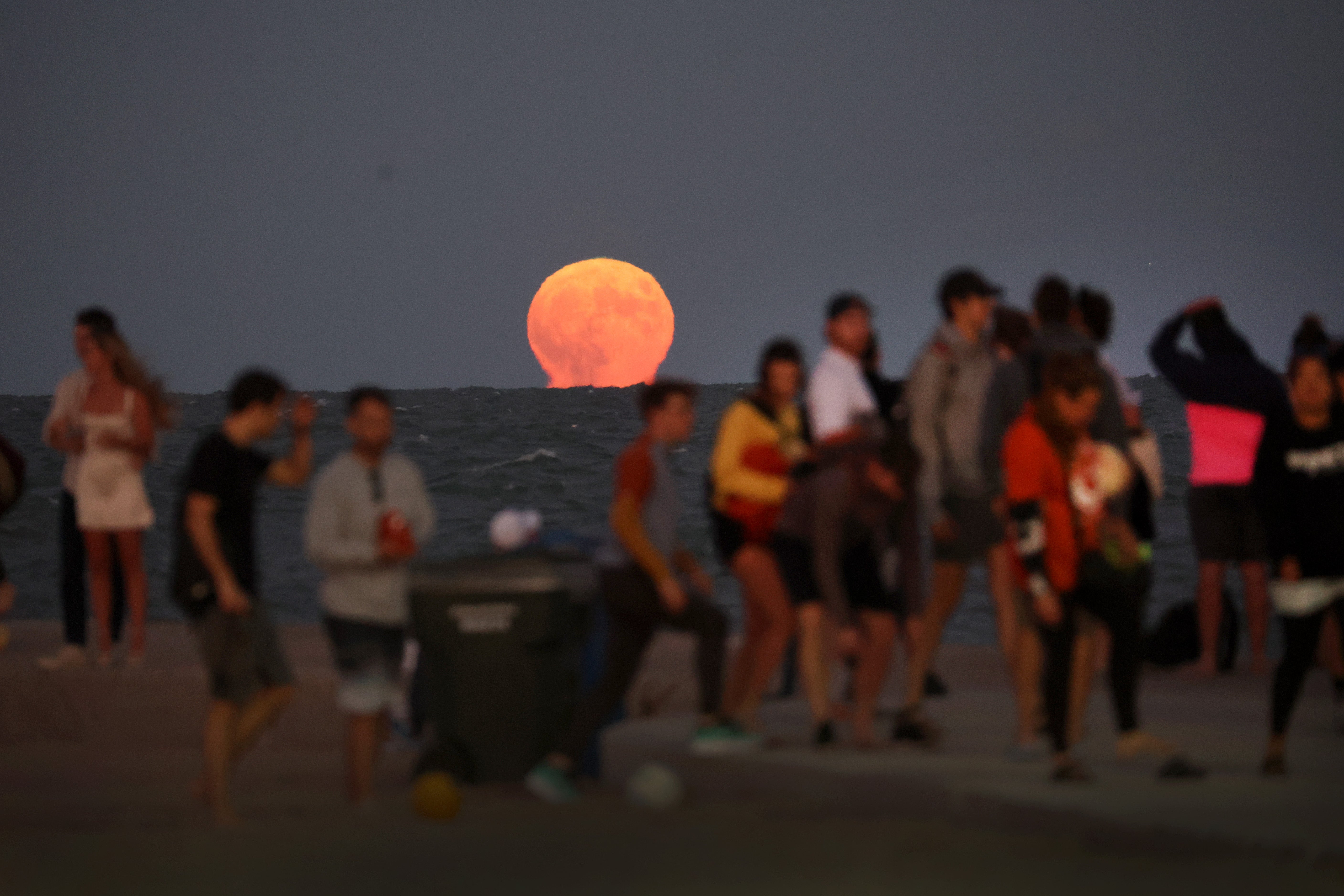 Varias personas contemplan desde la playa North Avenue Beach, en Chicago, Illinois, la salida de la superluna azul en agosto de 2023. Este fin de semana se producirá una luna azul