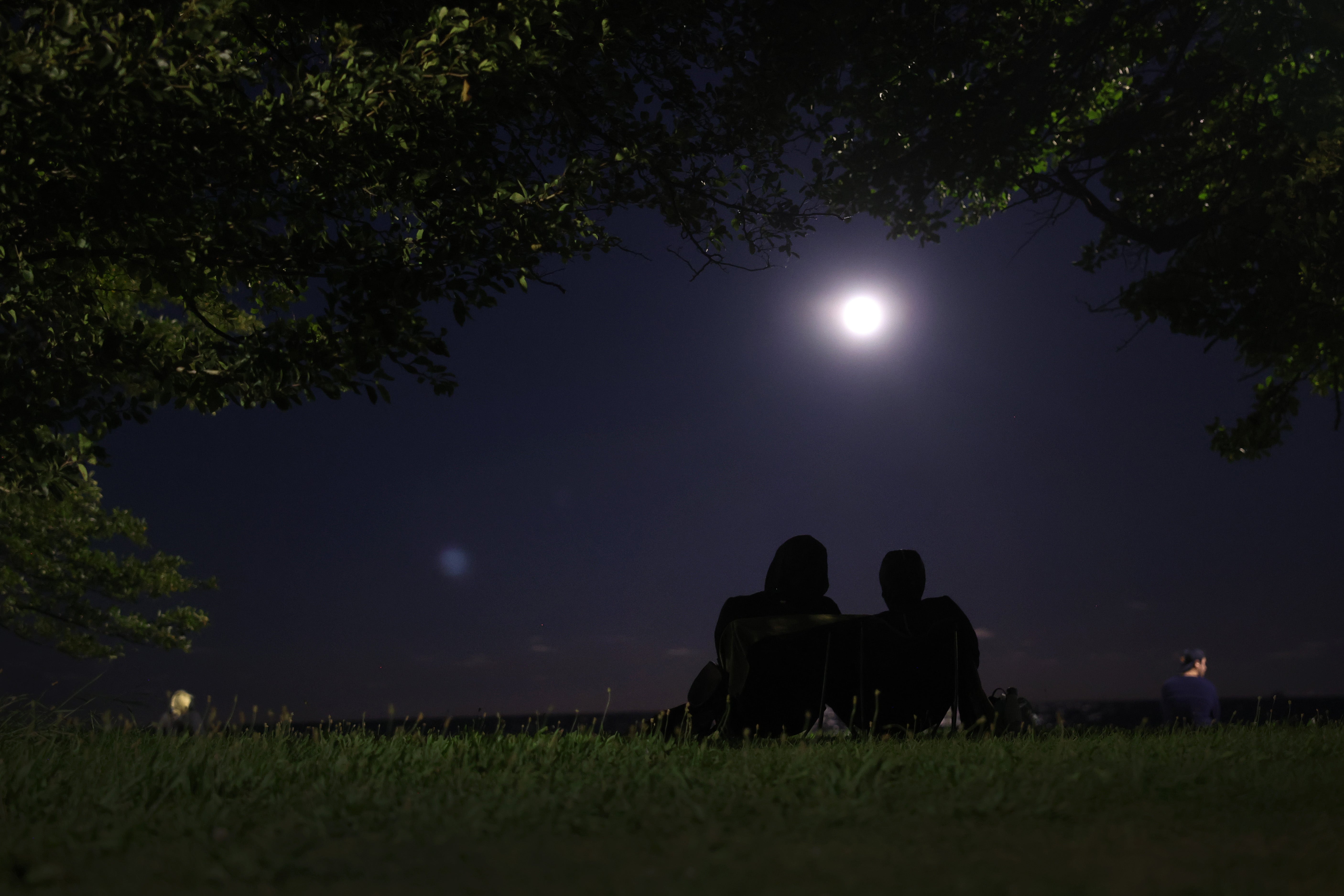 Dos personas contemplan la salida de la luna azul de agosto de 2023 en Chicago, Illinois. Para disfrutar de una vista más nítida del cielo nocturno, conviene evitar la contaminación lumínica
