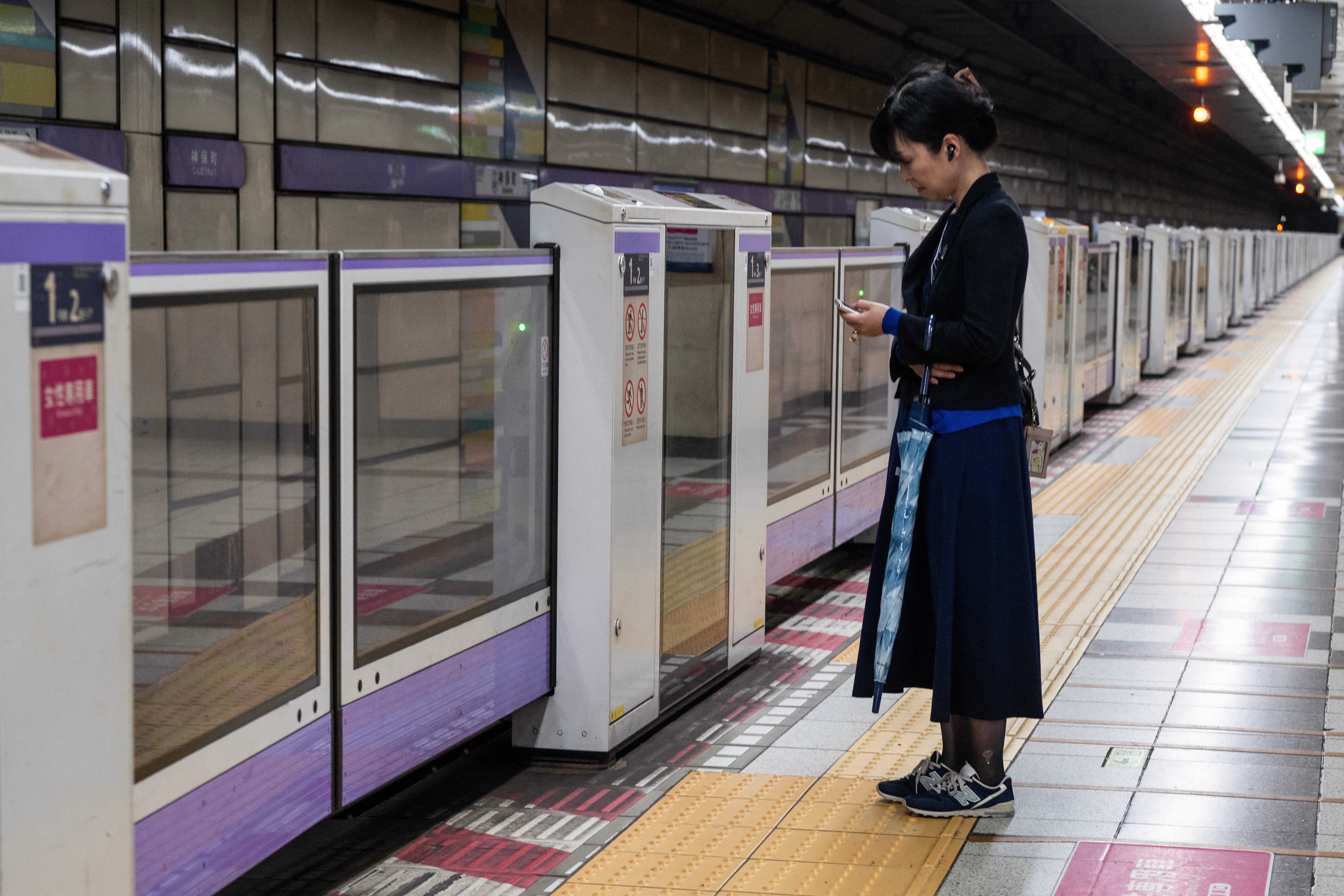 Una mujer con paraguas espera un tren en un andén vacío durante la hora pico mientras la tormenta tropical severa Jangmi azota Tokio