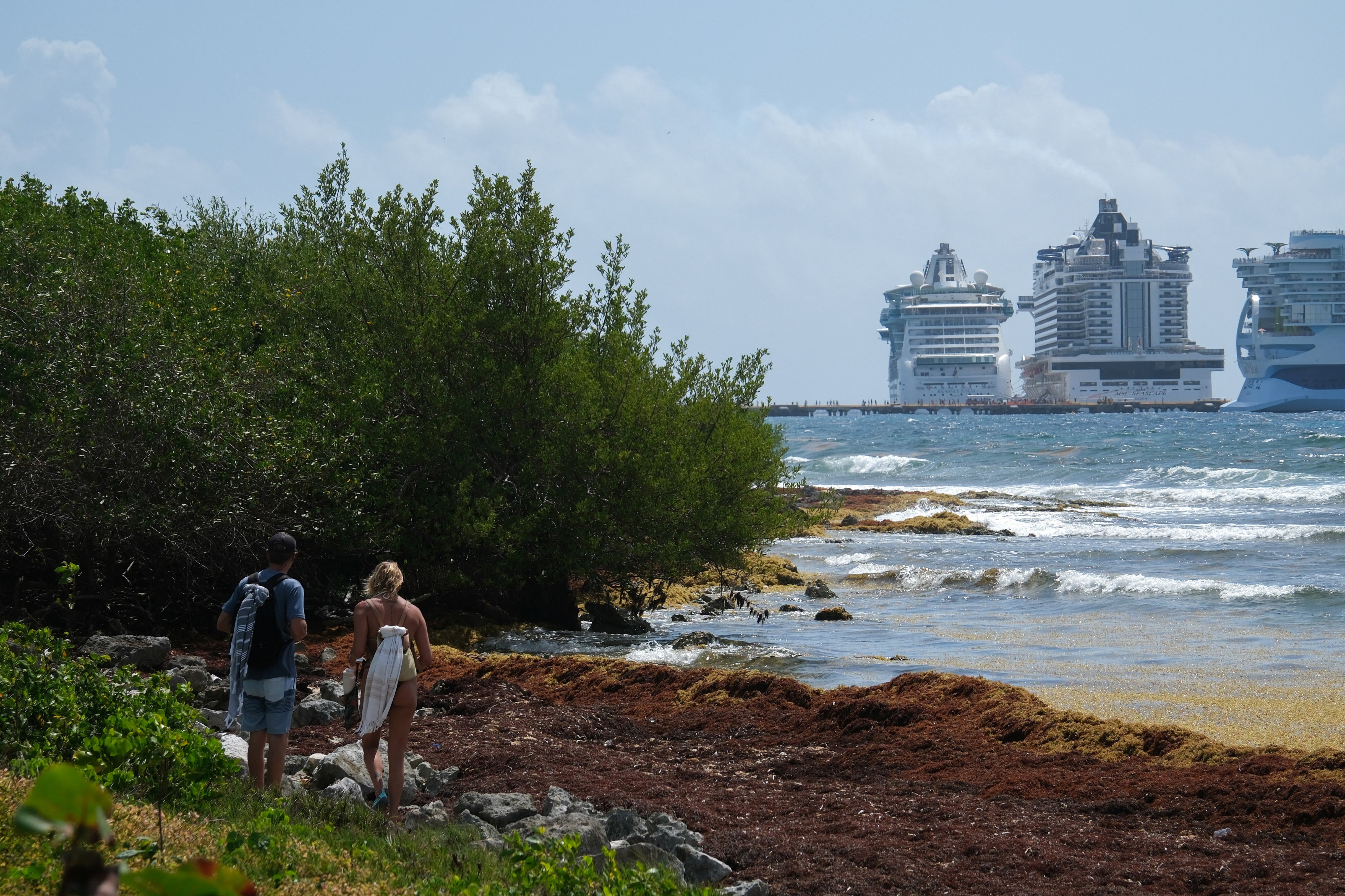Unos turistas pasean por la playa frente a tres cruceros: ‘Star of the Seas’ y ‘Radiance of the Seas’ de Royal Caribbean, y el ‘MSC Seascape’ de MSC Cruceros