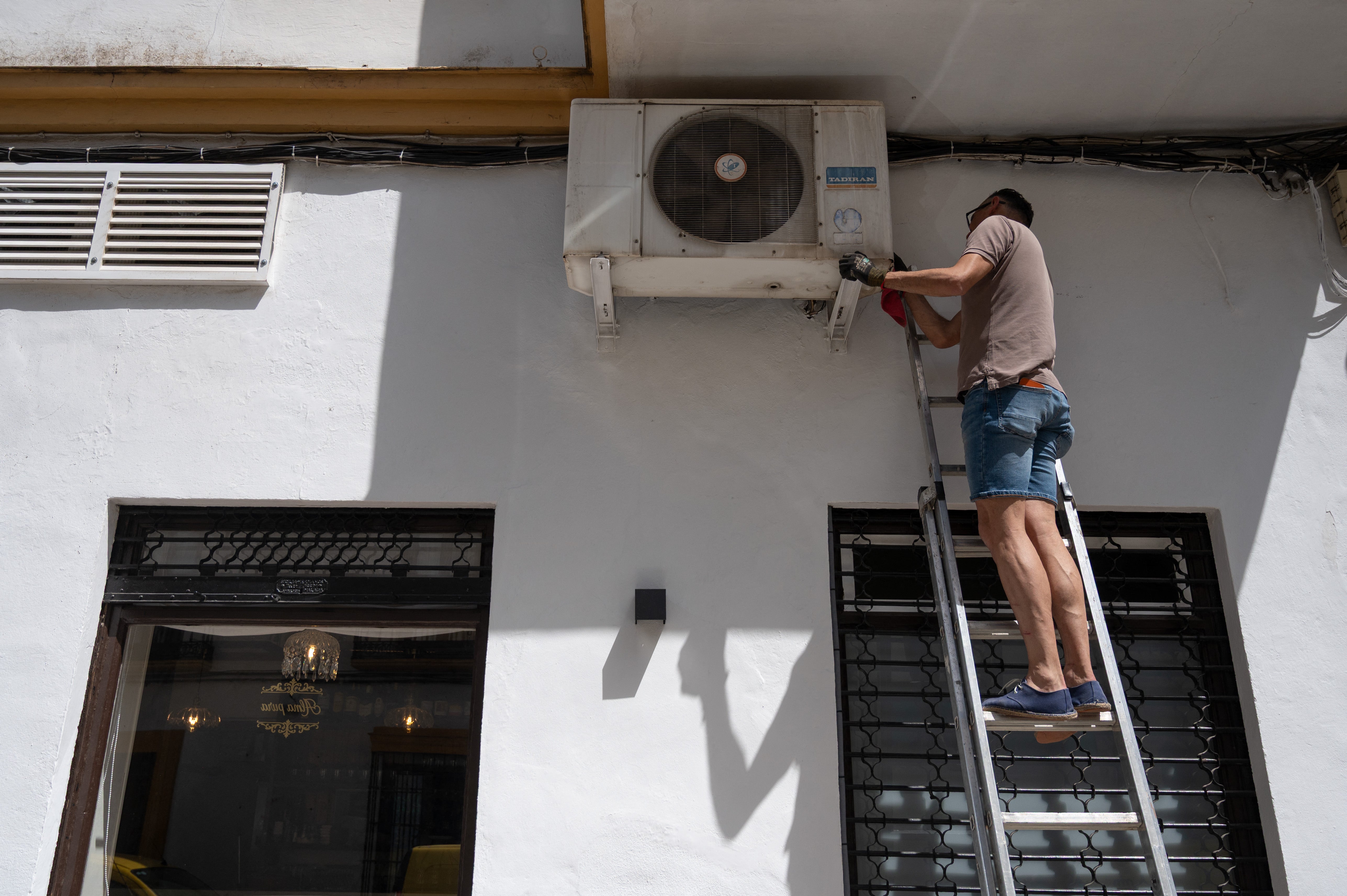 Un técnico repara un aparato de aire acondicionado en la fachada de un restaurante del centro de Ronda, en el sur de España
