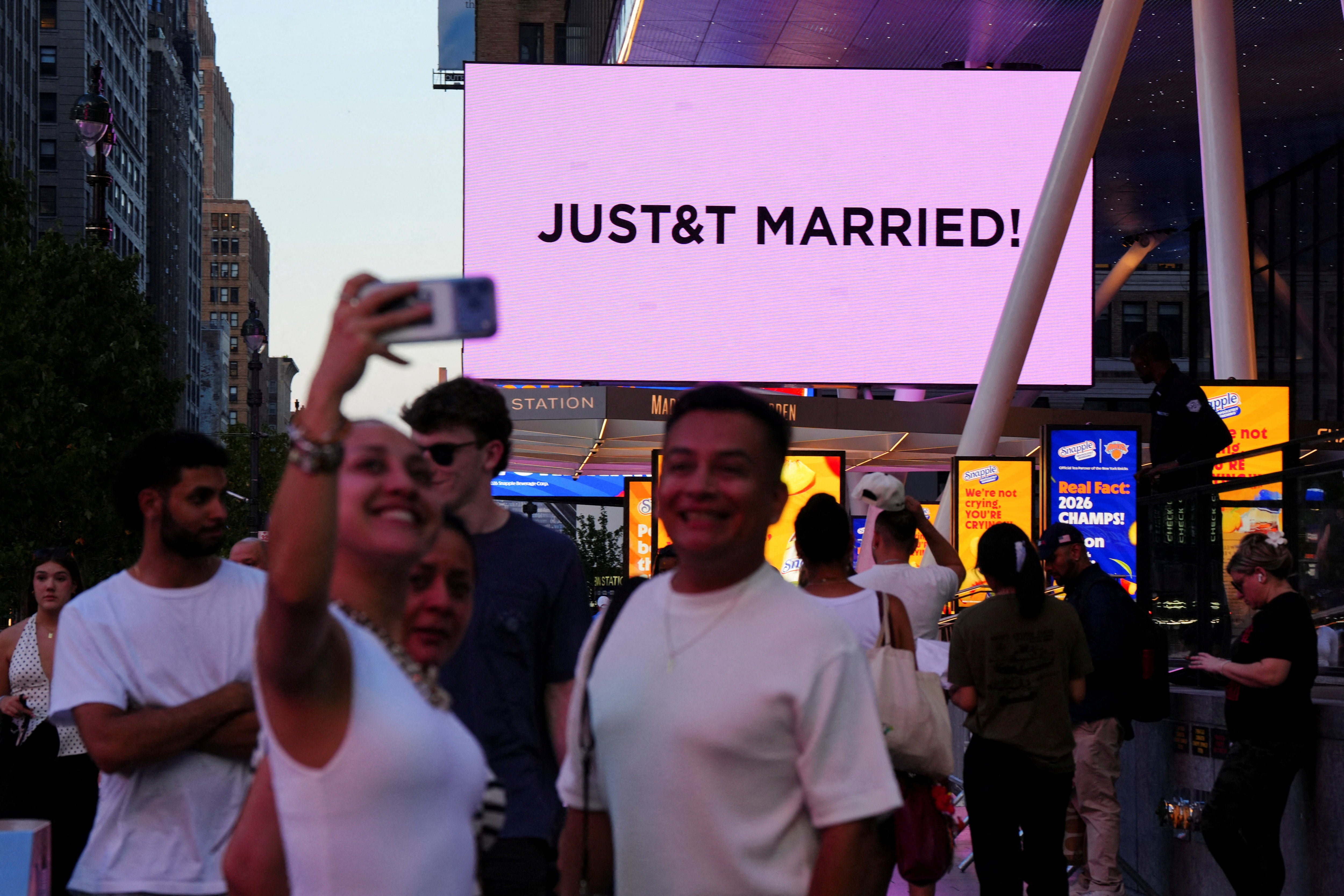 Los fans se hacen selfies frente al lugar de la boda de Swift y Kelce mientras se anuncia la noticia en pantallas gigantes situadas en el exterior del MSG
