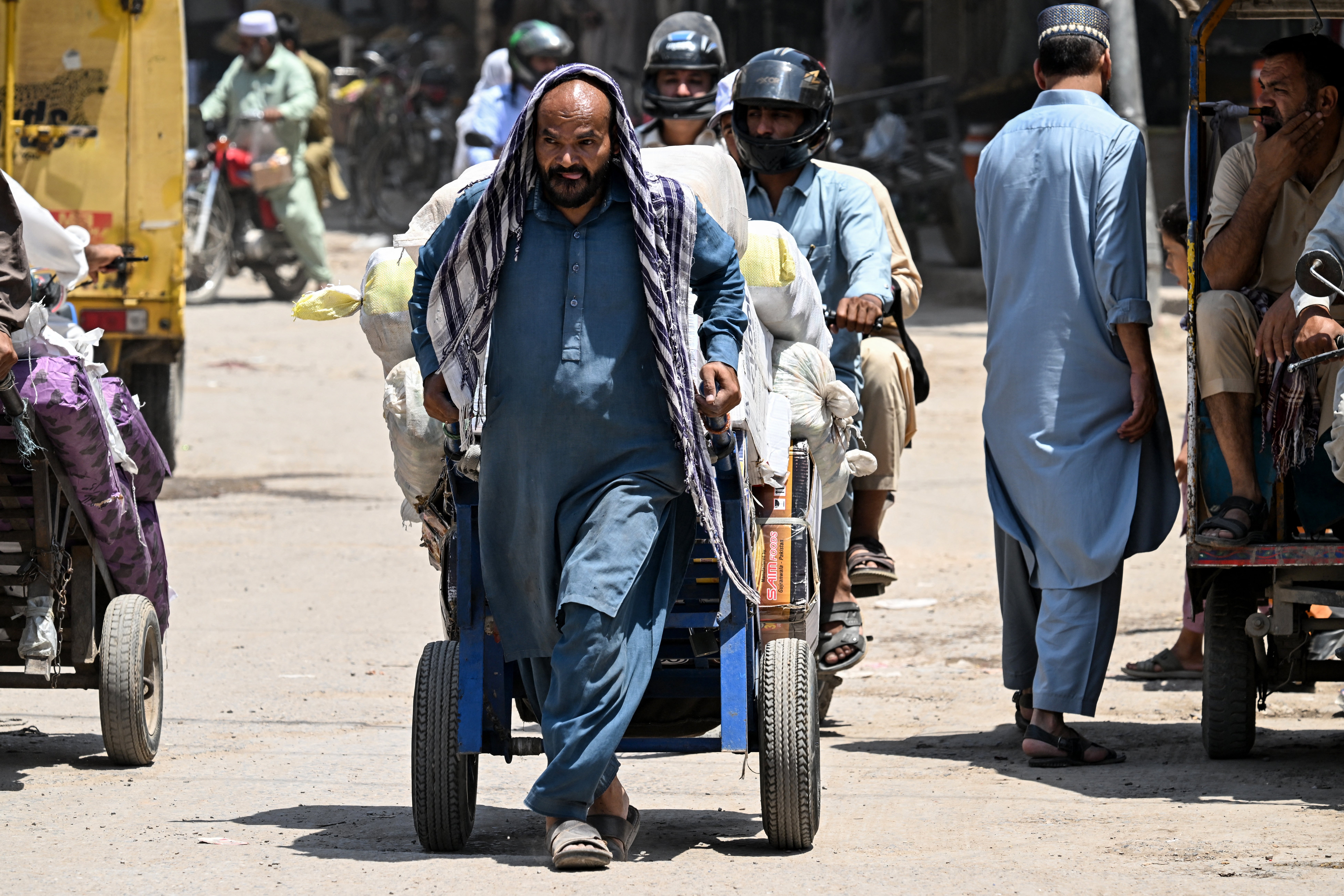 Un obrero se protege la cabeza con un paño mientras tira de una carretilla cargada en medio de una ola de calor en Rawalpindi, Pakistán