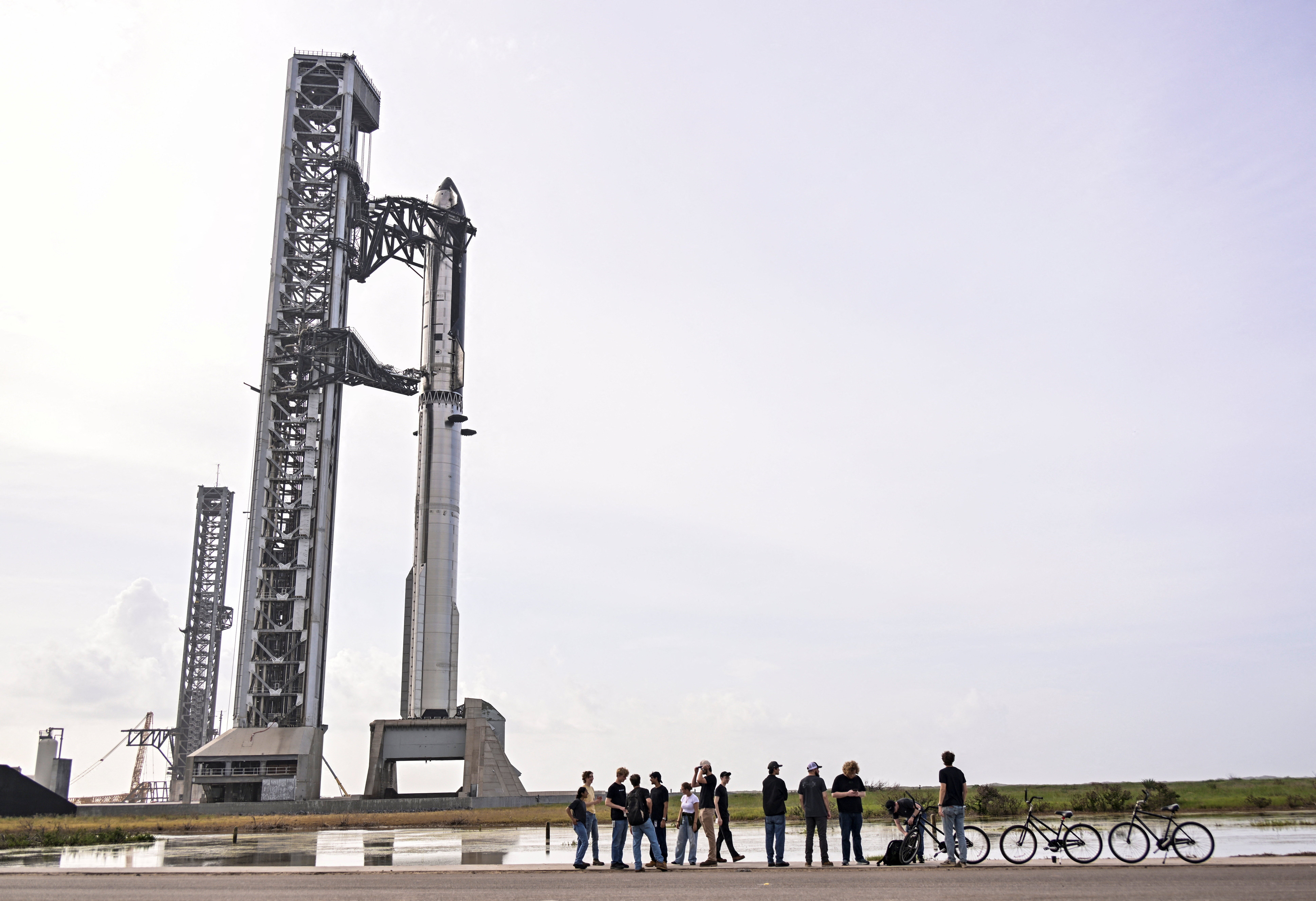 Empleados de SpaceX se reflejan en el panel lateral de una Tesla Cybertruck mientras se reúnen cerca de la nave Starship y el propulsor Super Heavy V3 en la plataforma 2, antes del decimotercer vuelo de prueba desde el complejo de lanzamiento de SpaceX en Starbase, Texas, el 16 de julio de 2026