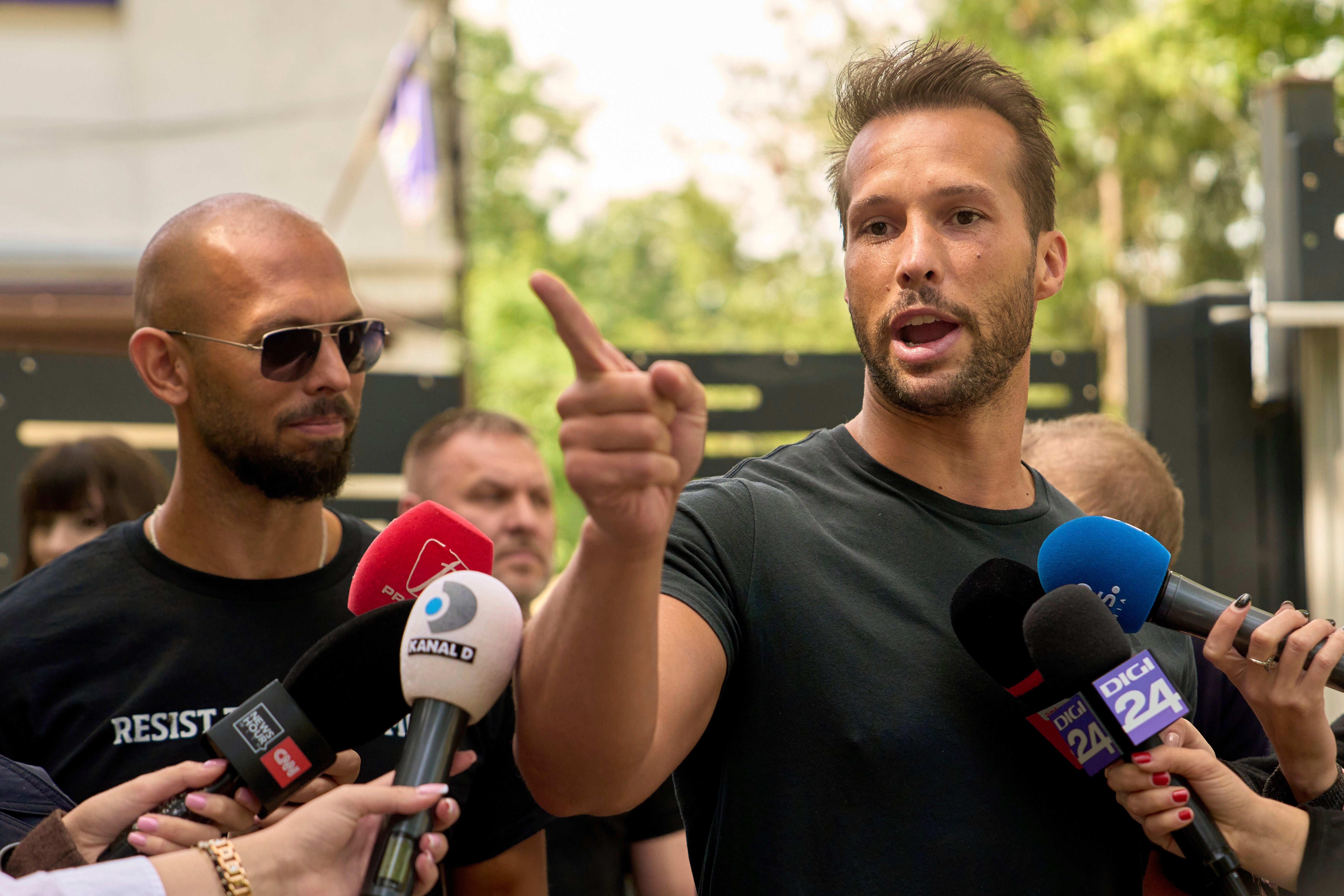 Andrew Tate, a la izquierda, observa a su hermano Tristan mientras habla frente a una comisaría en Voluntari, Rumania, el 21 de mayo de 2025