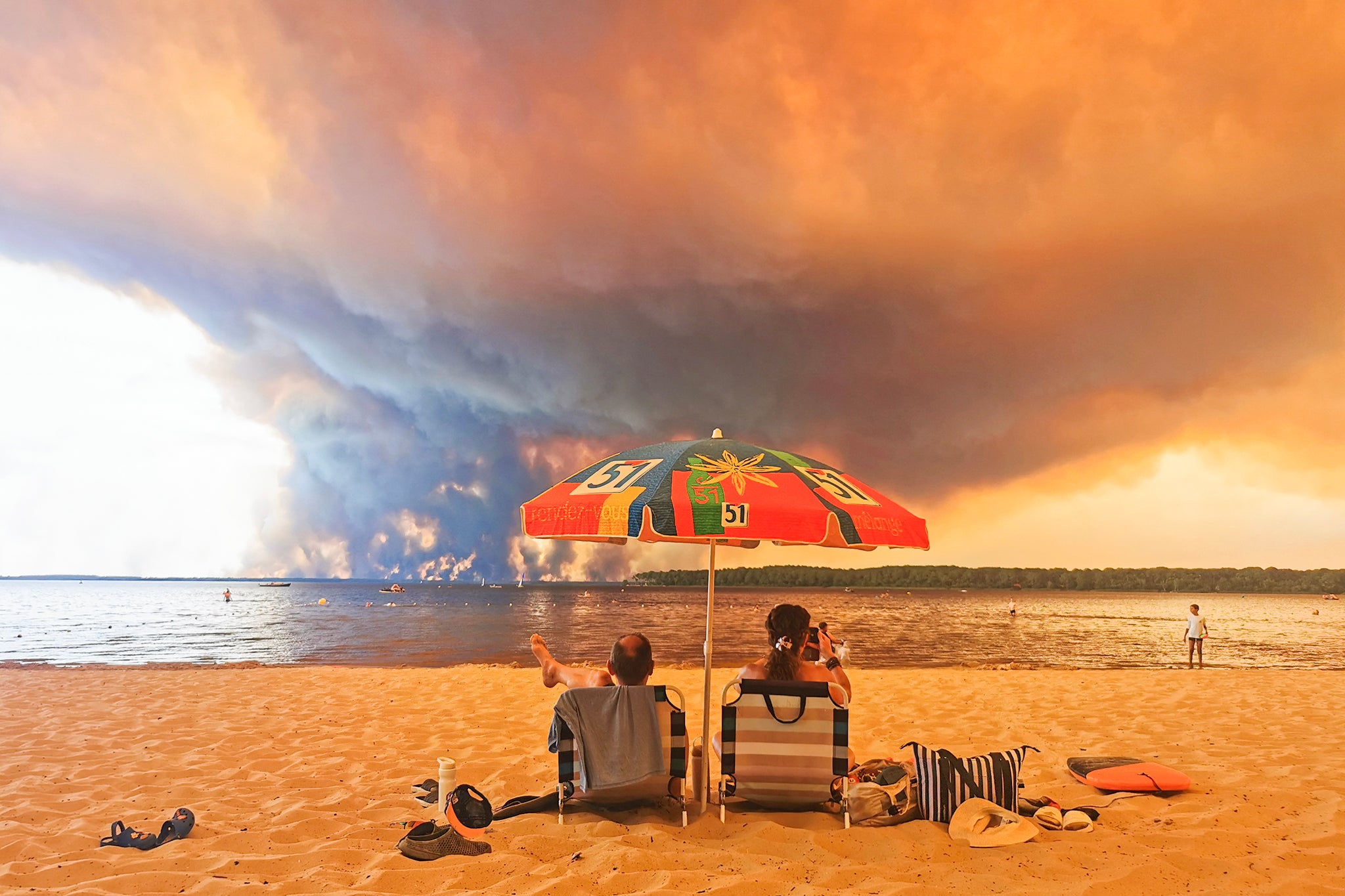 Bañistas descansan en la playa de Moutchic, en Lacanau (suroeste de Francia), mientras una columna de humo de un incendio forestal se eleva en el horizonte