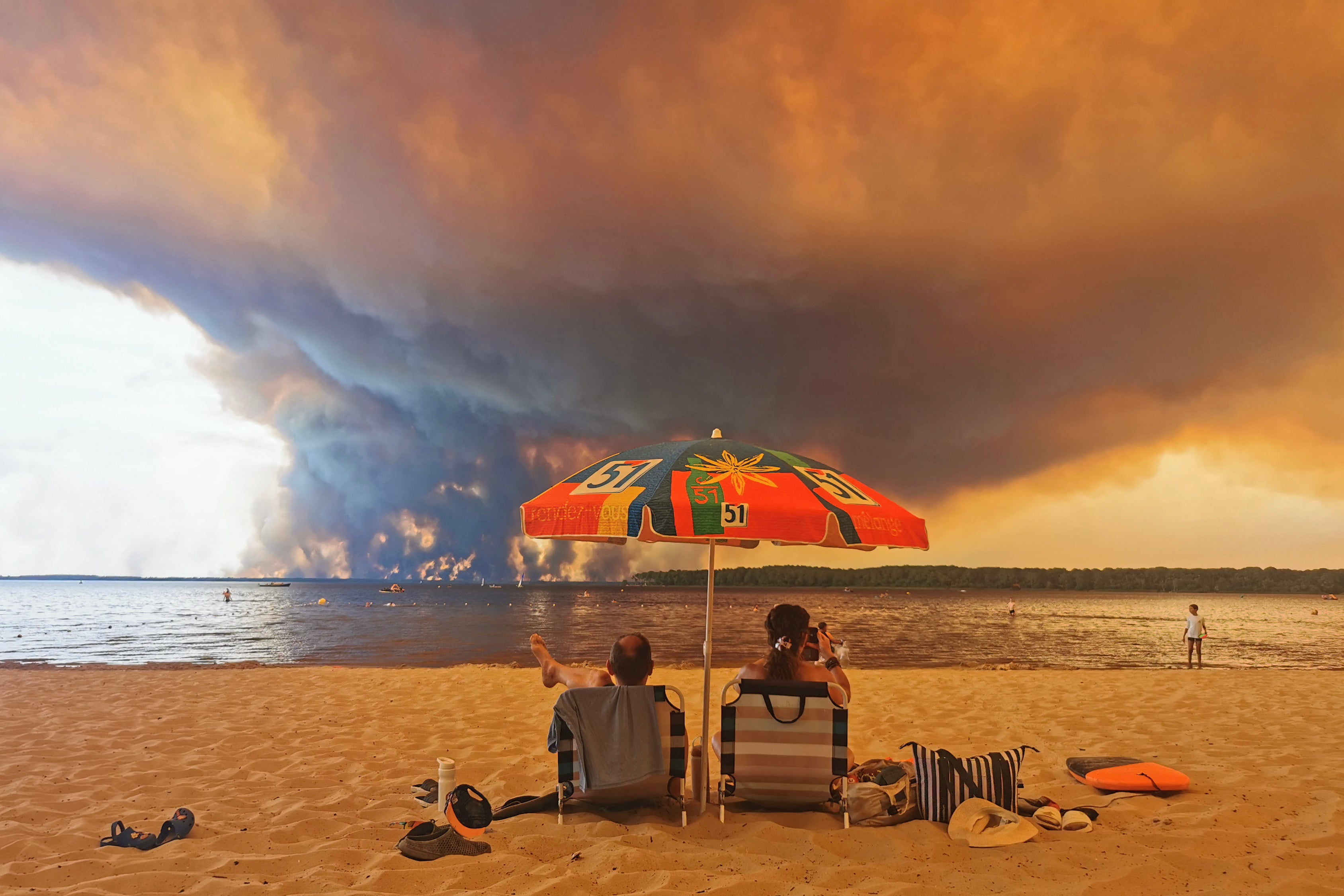 Bañistas permanecen en la playa de Moutchic, en Lacanau, al suroeste de Francia, mientras una enorme nube de humo se eleva por un incendio forestal