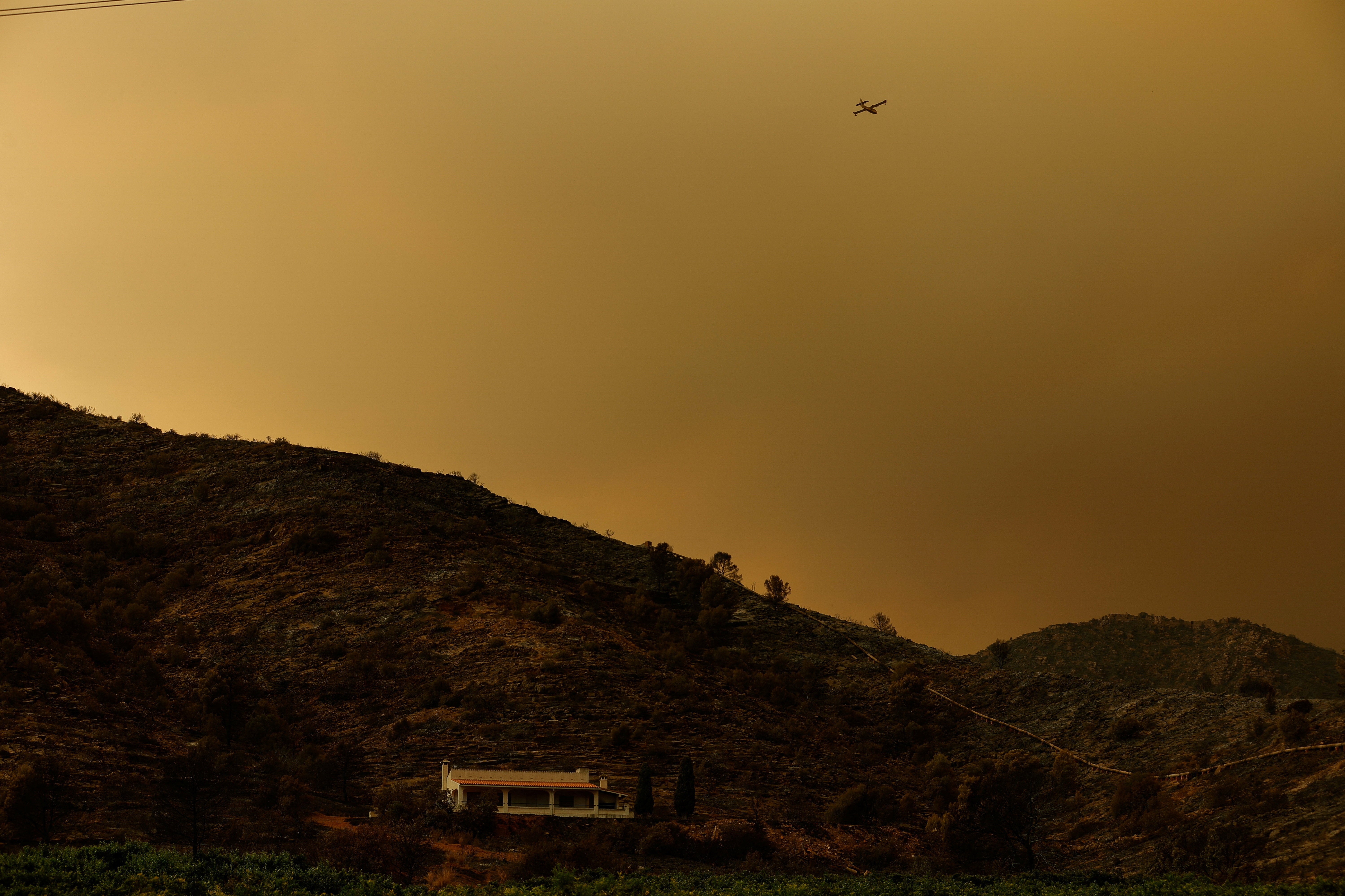 Un avión sobrevuela la zona mientras el humo se eleva desde un incendio forestal en La Vall d’Uixo, Castellón, España