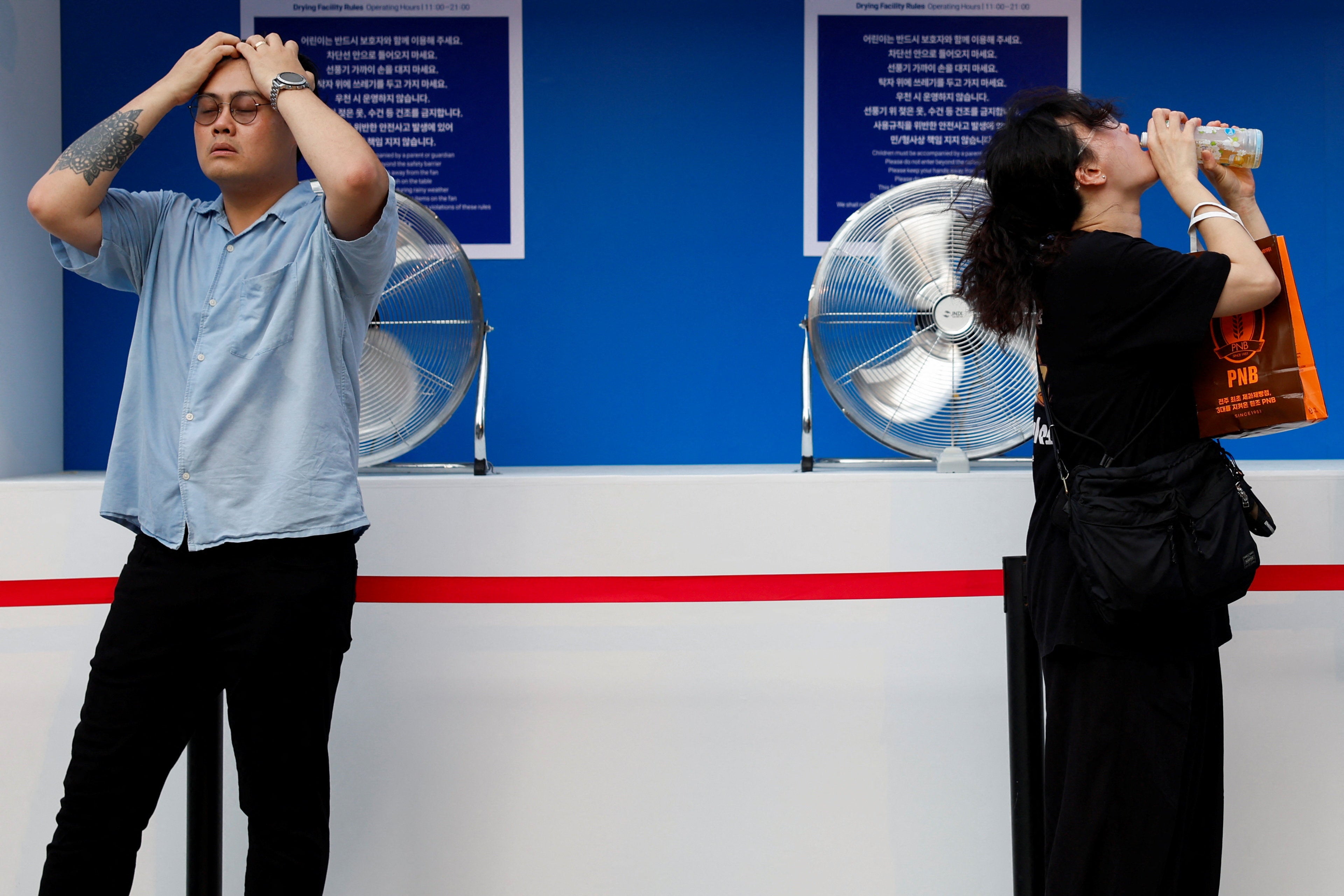 Las personas se refrescan frente a ventiladores durante una ola de calor en Seúl