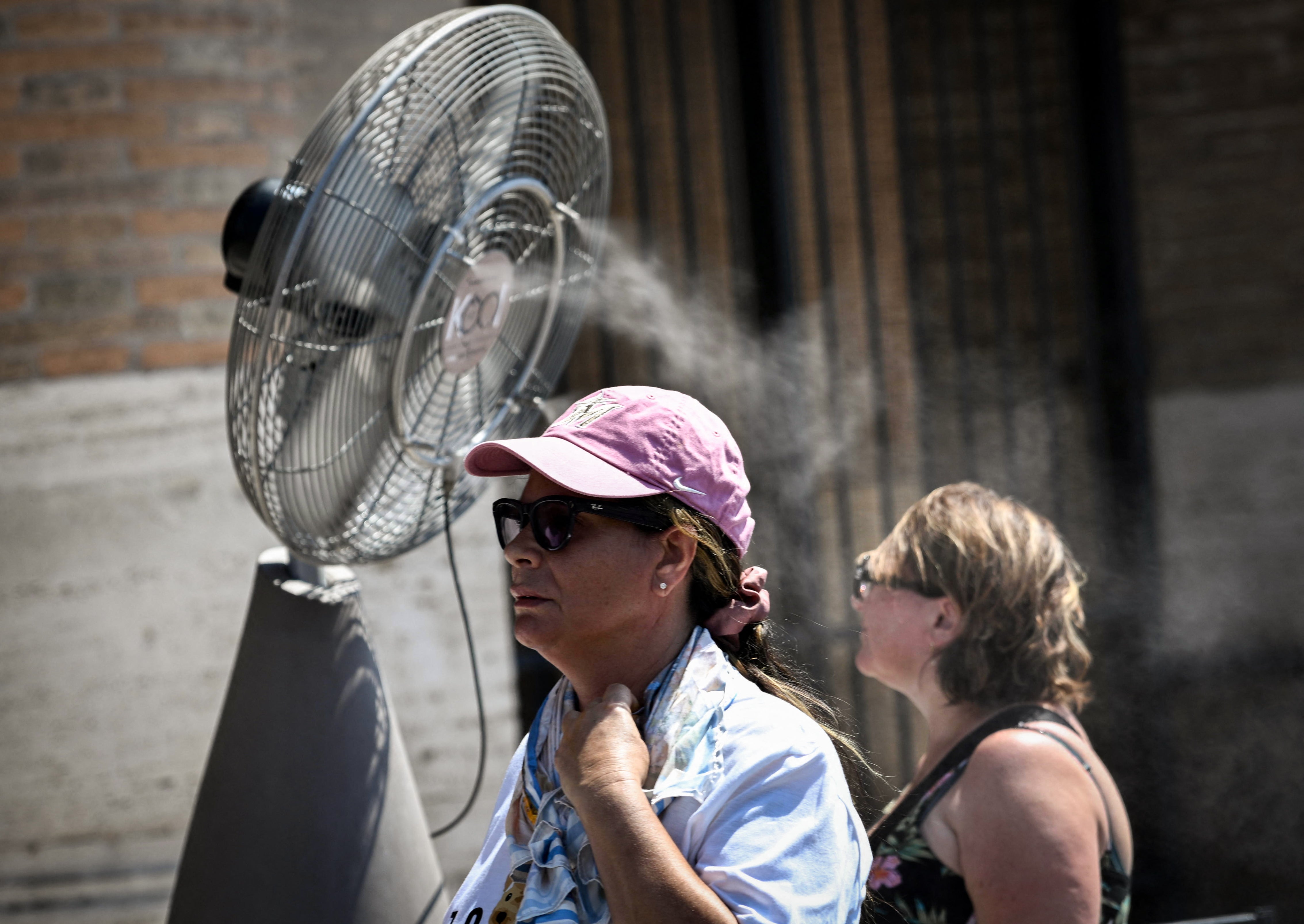 Turistas se refrescan junto a un ventilador con nebulizador de agua durante la ola de calor en el Coliseo de Roma, el 6 de agosto de 2026