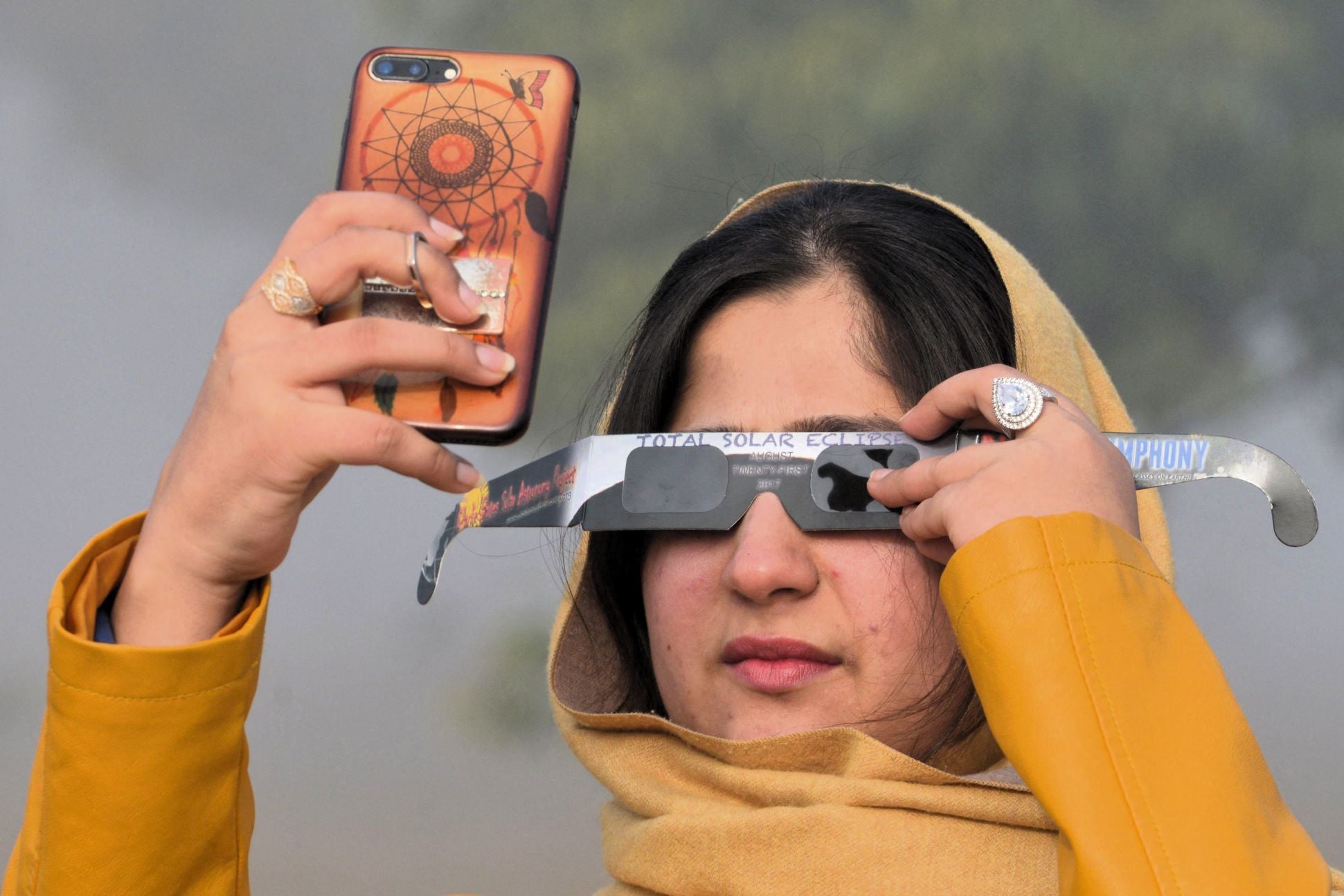 Una mujer utiliza lentes con filtro solar mientras toma una foto de un eclipse solar con su teléfono inteligente en Islamabad, Pakistán, el 26 de diciembre de 2019