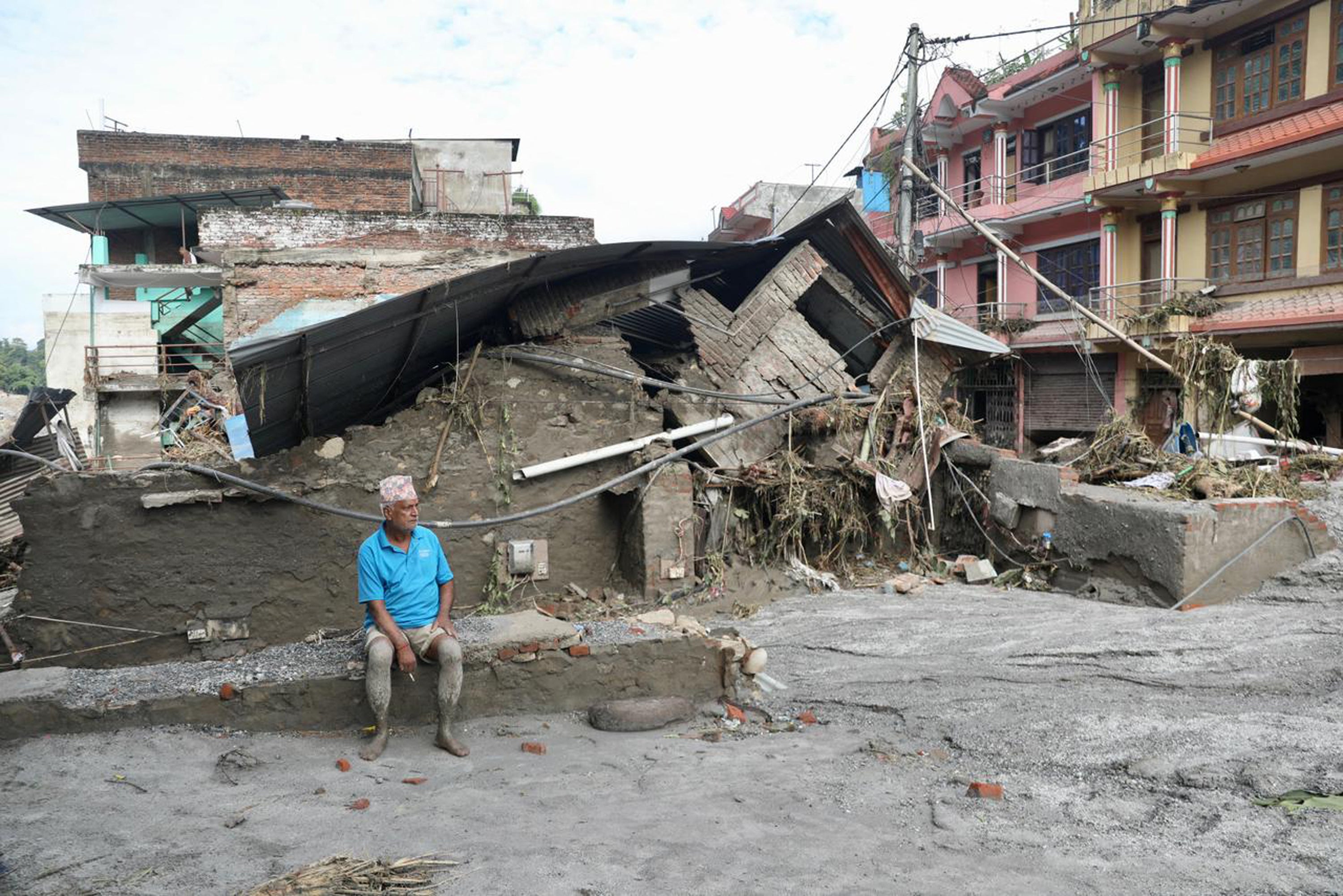 Un vecino se sienta junto a una casa derrumbada y cubierta de lodo tras las crecidas repentinas registradas en Devighat, en el municipio de Bidur, en el distrito de Nuwakot (Nepal)