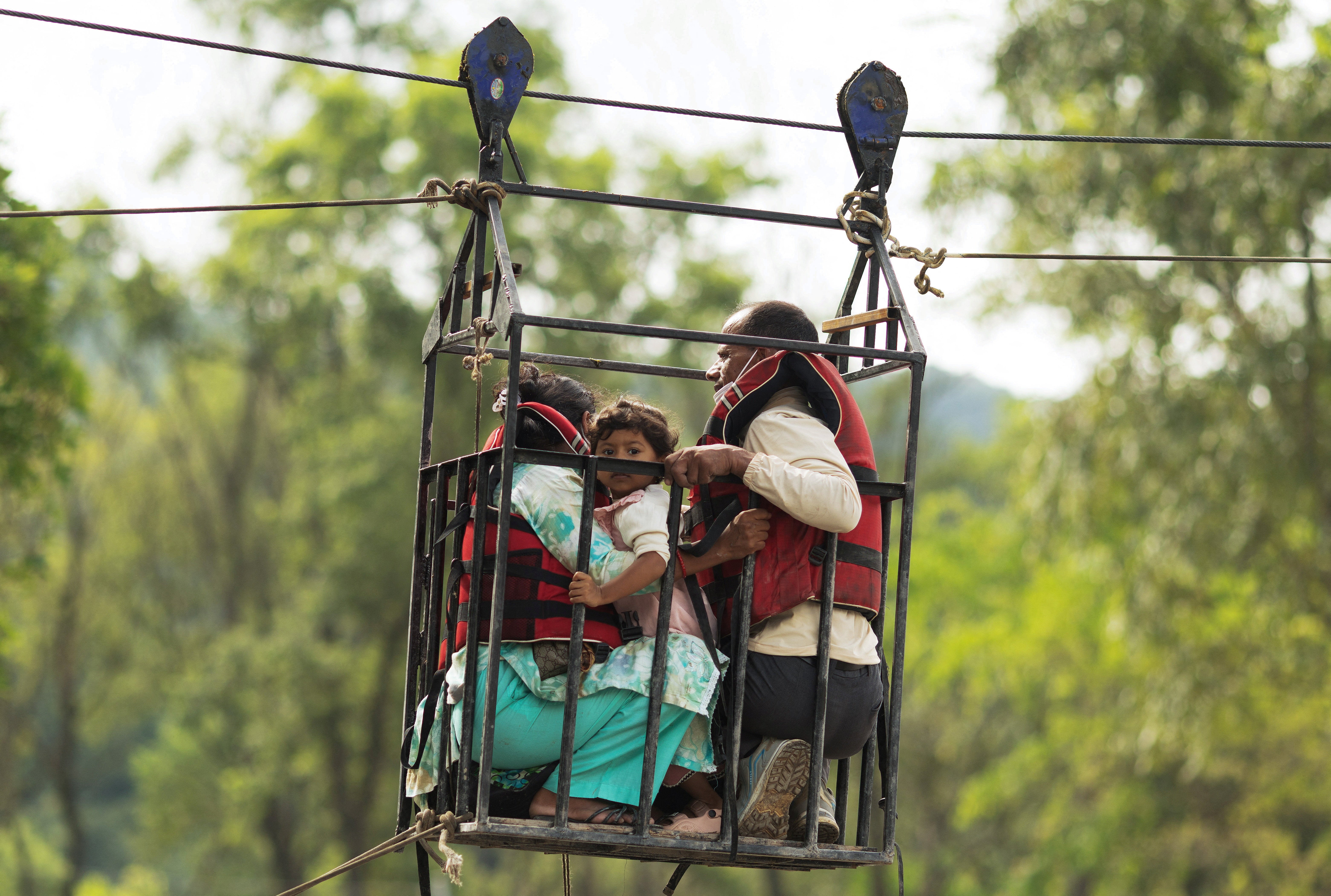 Madhu Sudan Sapkota, de 50 años; Sangita Kunwar, de 25; y su hija Nekisha Rijal, de 3, se sujetan a una jaula en una tirolesa improvisada para cruzar el río Trishuli desde Koloni, tras las mortales inundaciones repentinas