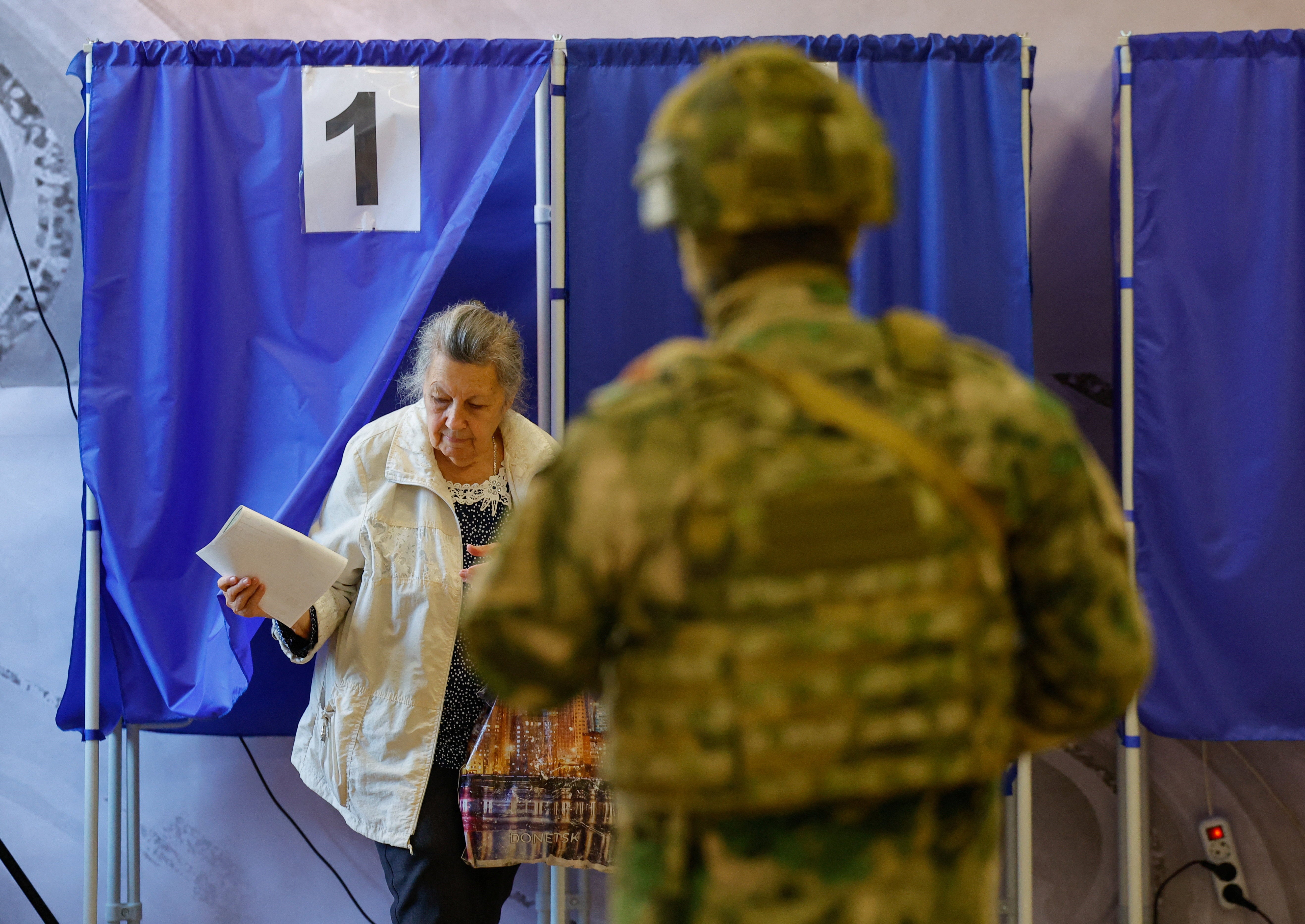 Una mujer sale de una cabina de votación con su papeleta en Donetsk