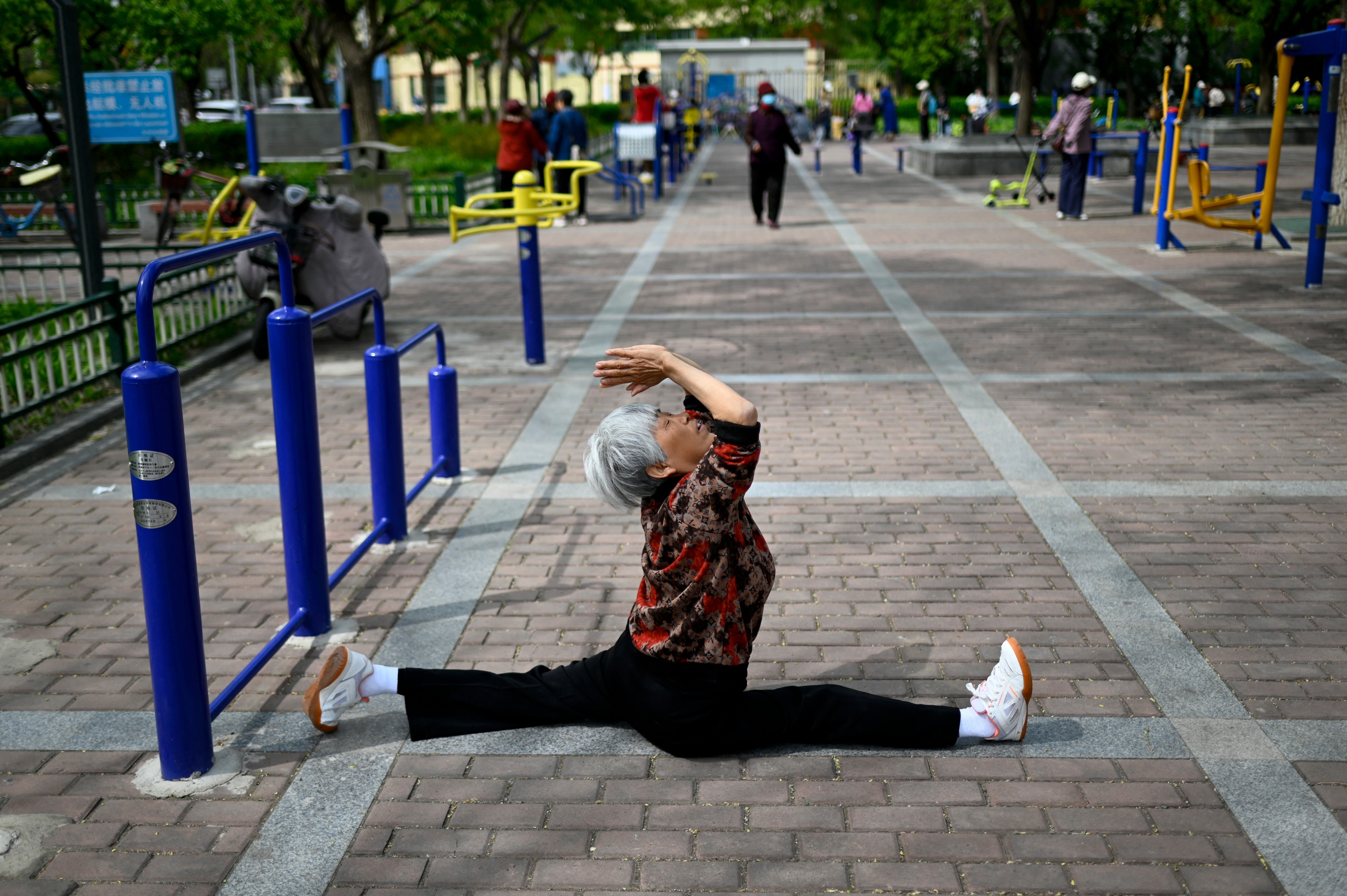 Una mujer mayor hace ejercicio en un parque público junto a una calle de Beijing