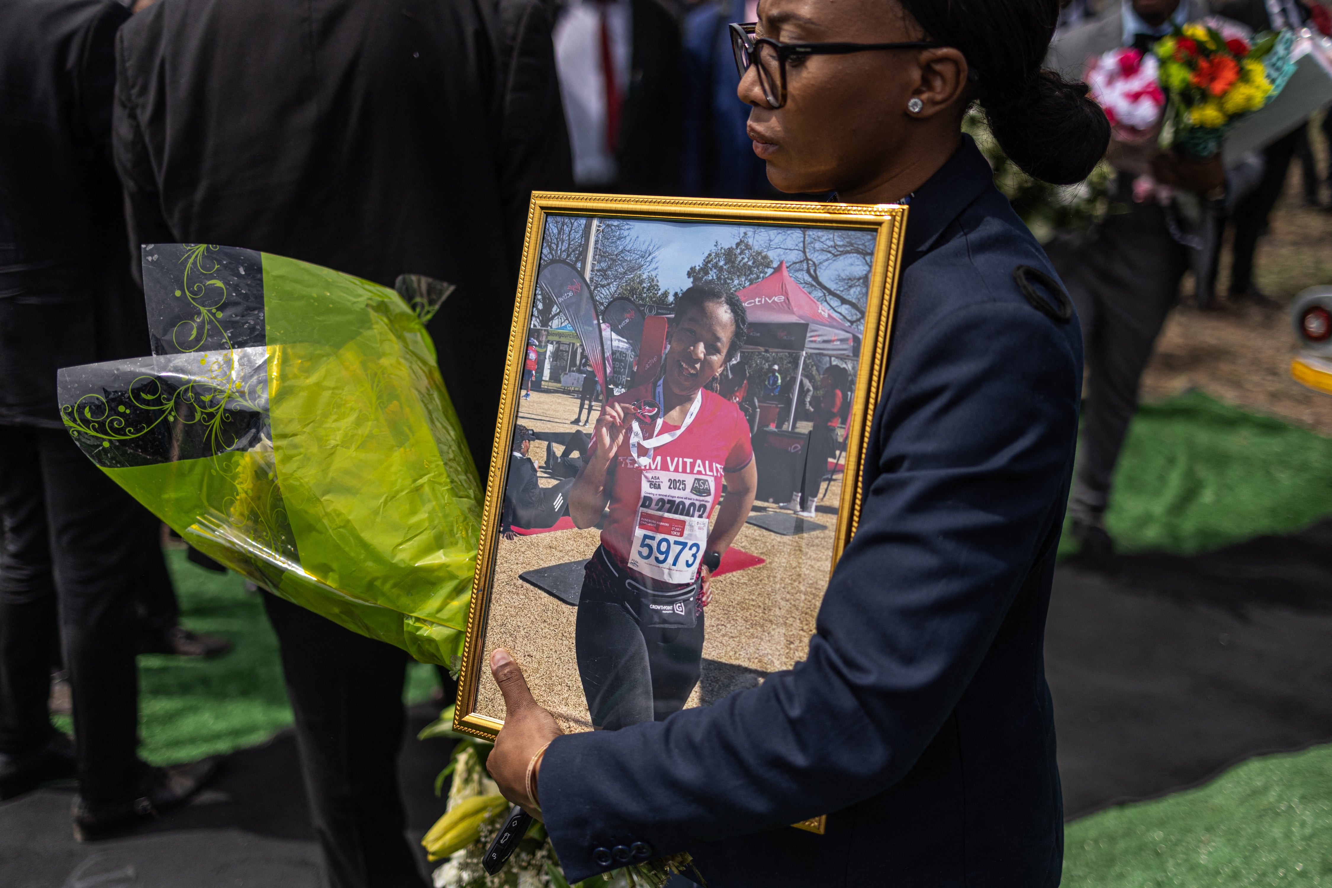 Una mujer sostiene un ramo de flores y un retrato de Elizabeth Moselakgomo