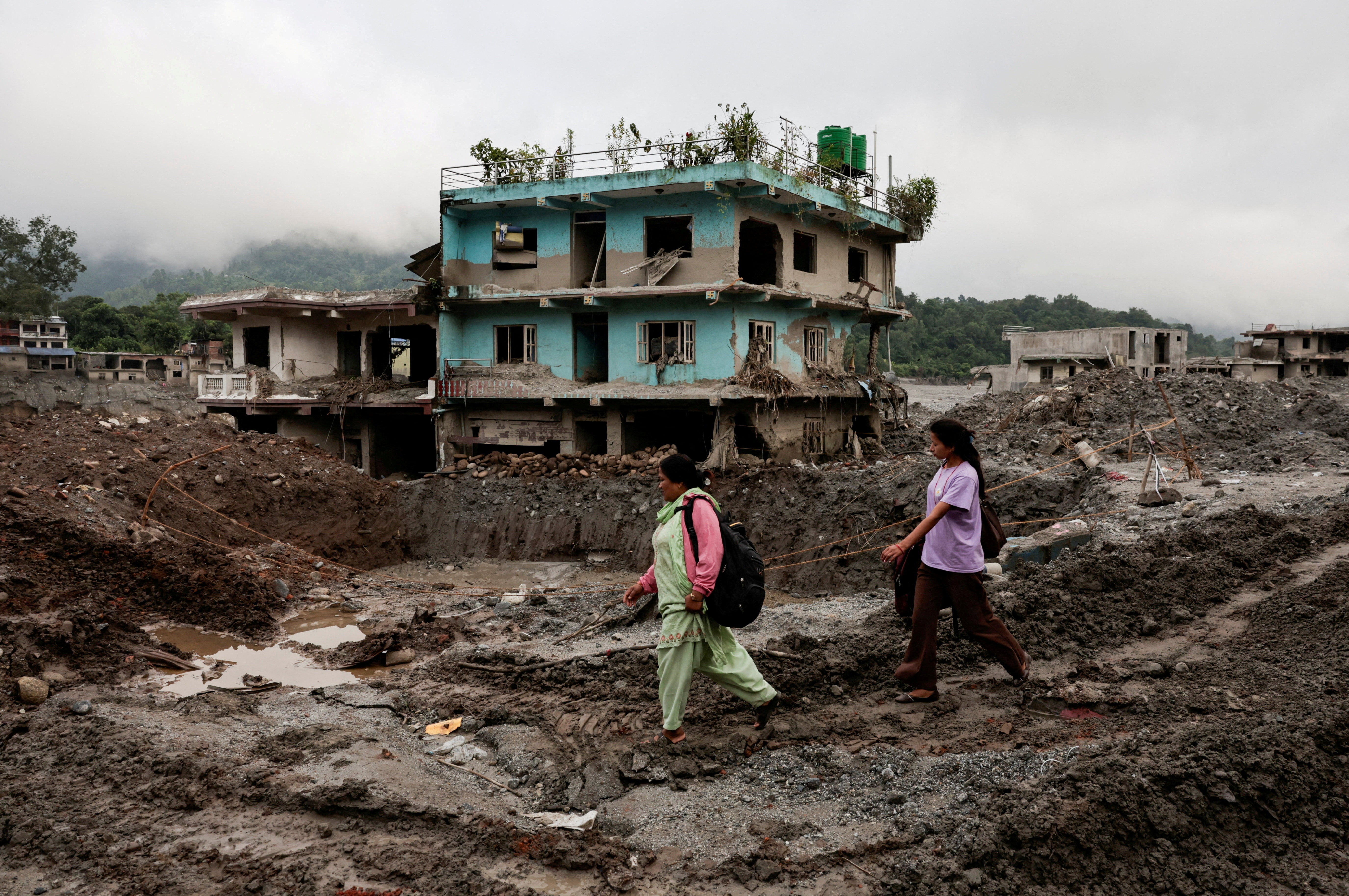 La gente pasa junto a casas dañadas tras las mortíferas riadas repentinas y un deslizamiento de tierra en Devighat, en el distrito de Nuwakot, Nepal