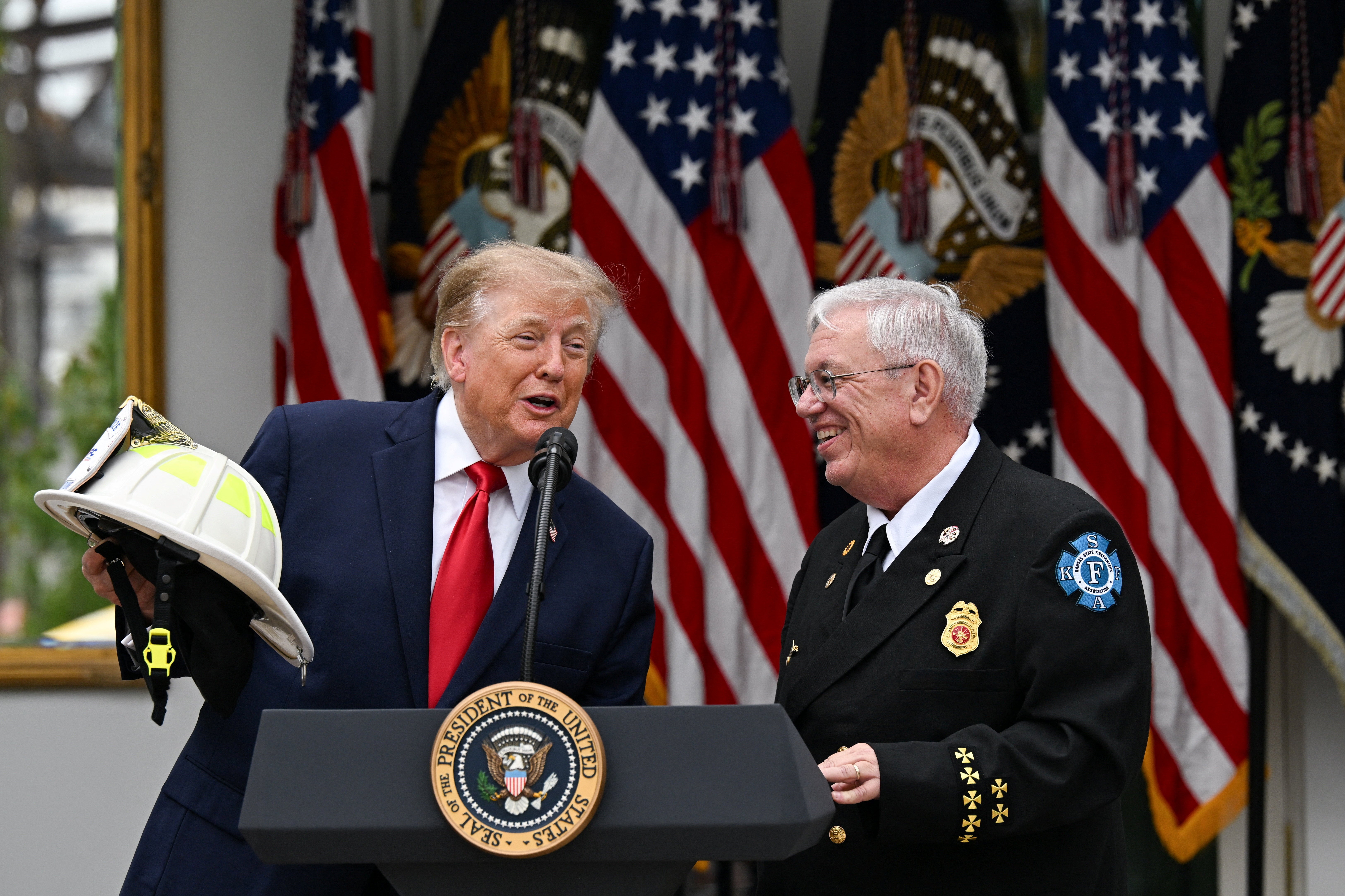El presidente del Consejo Nacional de Bomberos Voluntarios, el jefe Steve Hirsch, le entrega un casco de bombero a Trump durante el almuerzo en el Jardín de las Rosas