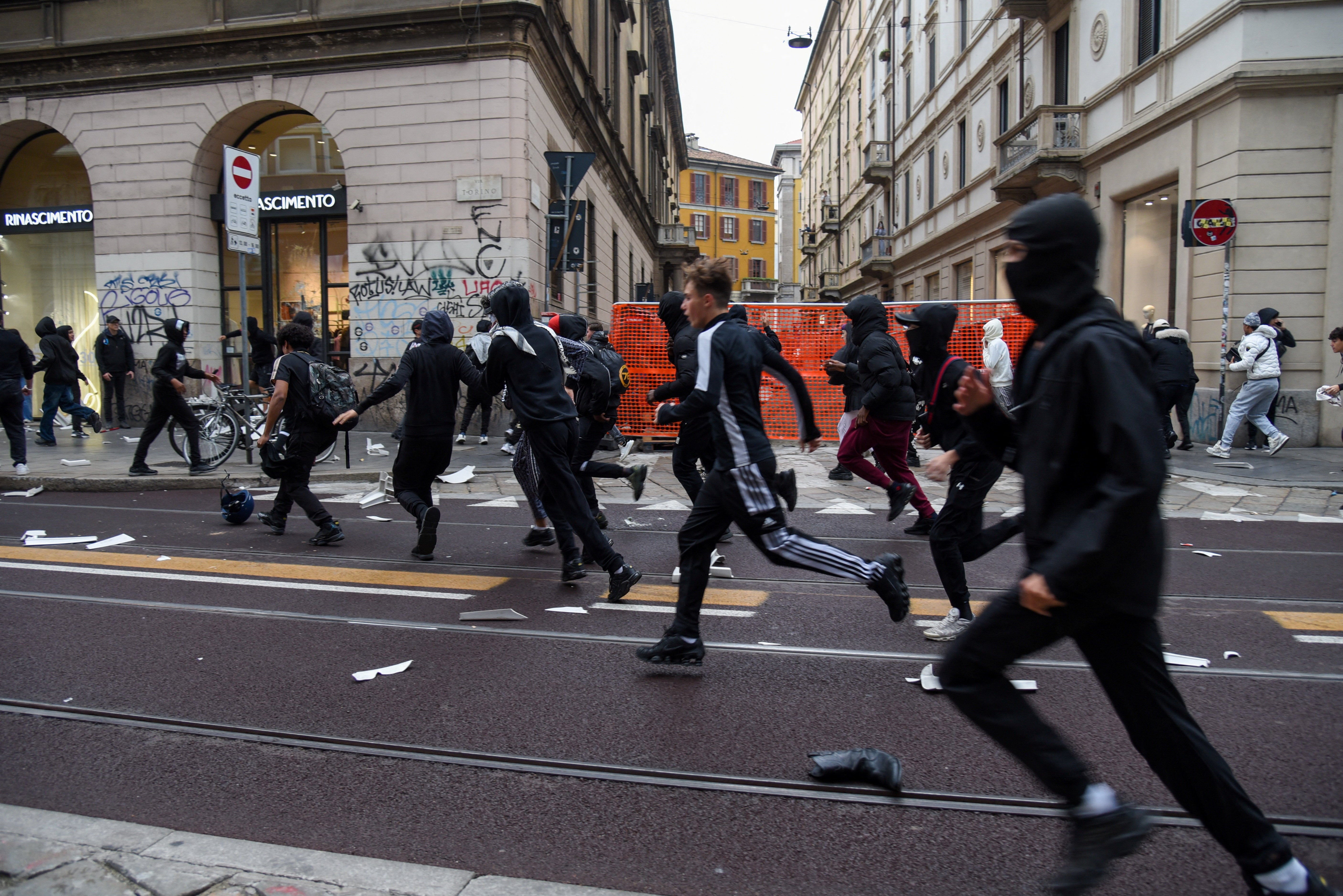 Manifestantes corren por una calle cubierta de escombros durante una protesta contra el deterioro de los servicios públicos y el aumento del costo de vida en Milán, el domingo