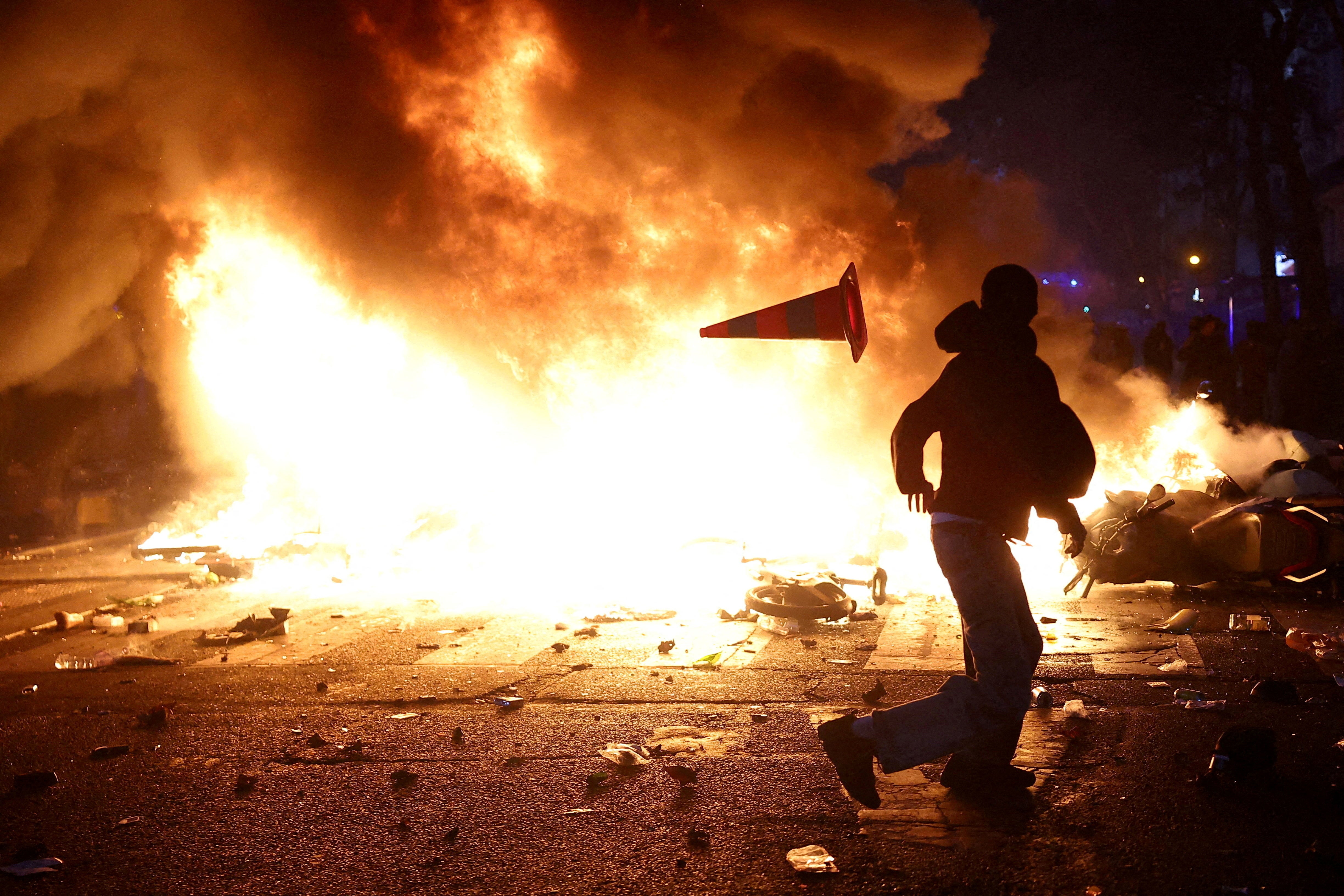 Un hombre lanza un cono de tráfico de plástico contra una barricada en llamas en medio de los enfrentamientos que se produjeron durante una jornada de manifestaciones contra el costo de la vida y la subida de los precios del combustible en París, en el marco de las protestas a nivel nacional convocadas por el movimiento de los chalecos amarillos, a las que se sumaron estudiantes de secundaria y universitarios franceses, profesores y padres que exigían mejores condiciones escolares y medidas por parte del Gobierno, así como sindicatos, trabajadores, agricultores y jubilados. Francia, 17 de octubre de 2026