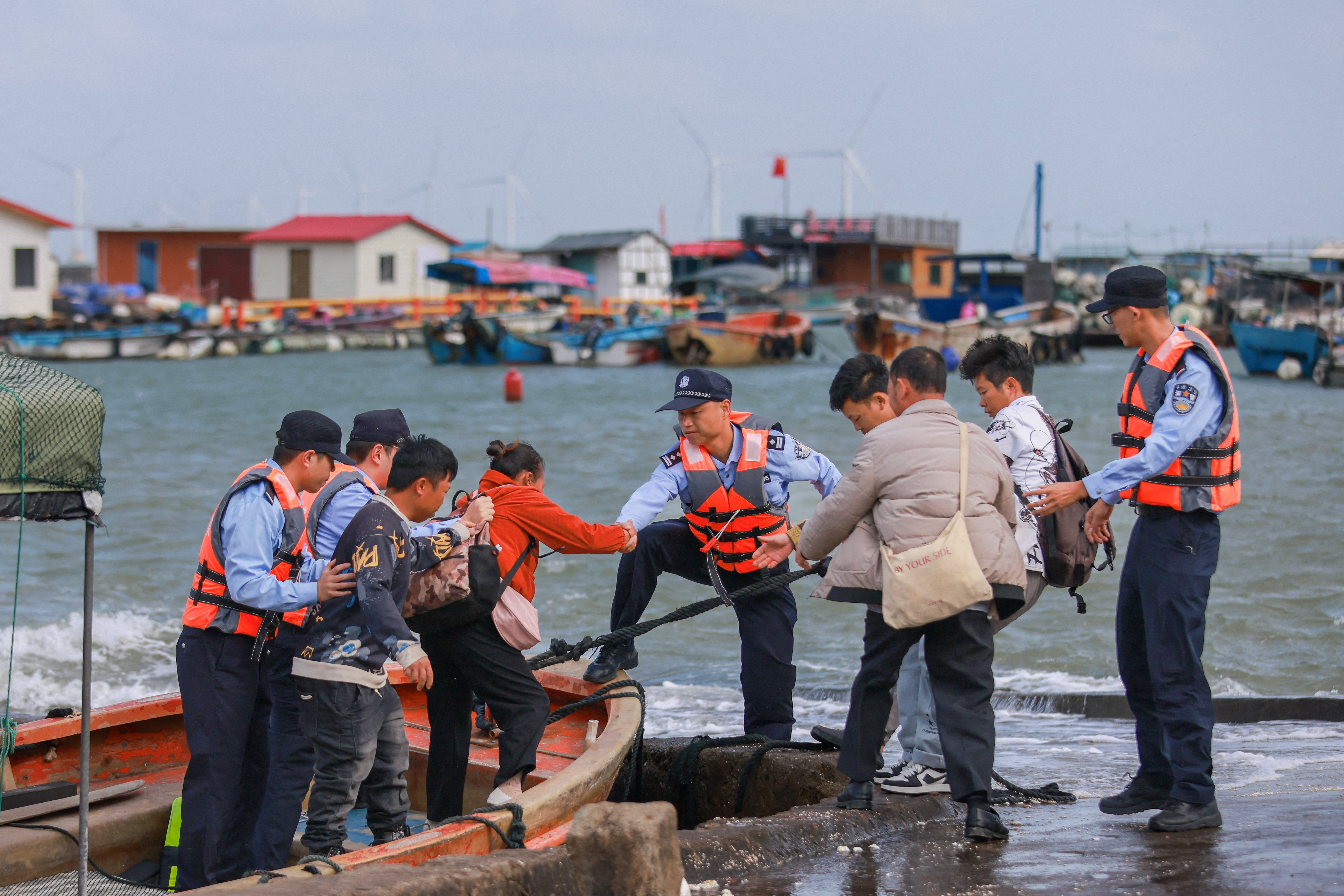 Agentes de policía ayudan a trabajadores de la acuicultura a desembarcar durante una evacuación ante la llegada del tifón Champi, en un muelle de la aldea de Longtou, en la provincia china de Fujian, el 22 de octubre de 2026