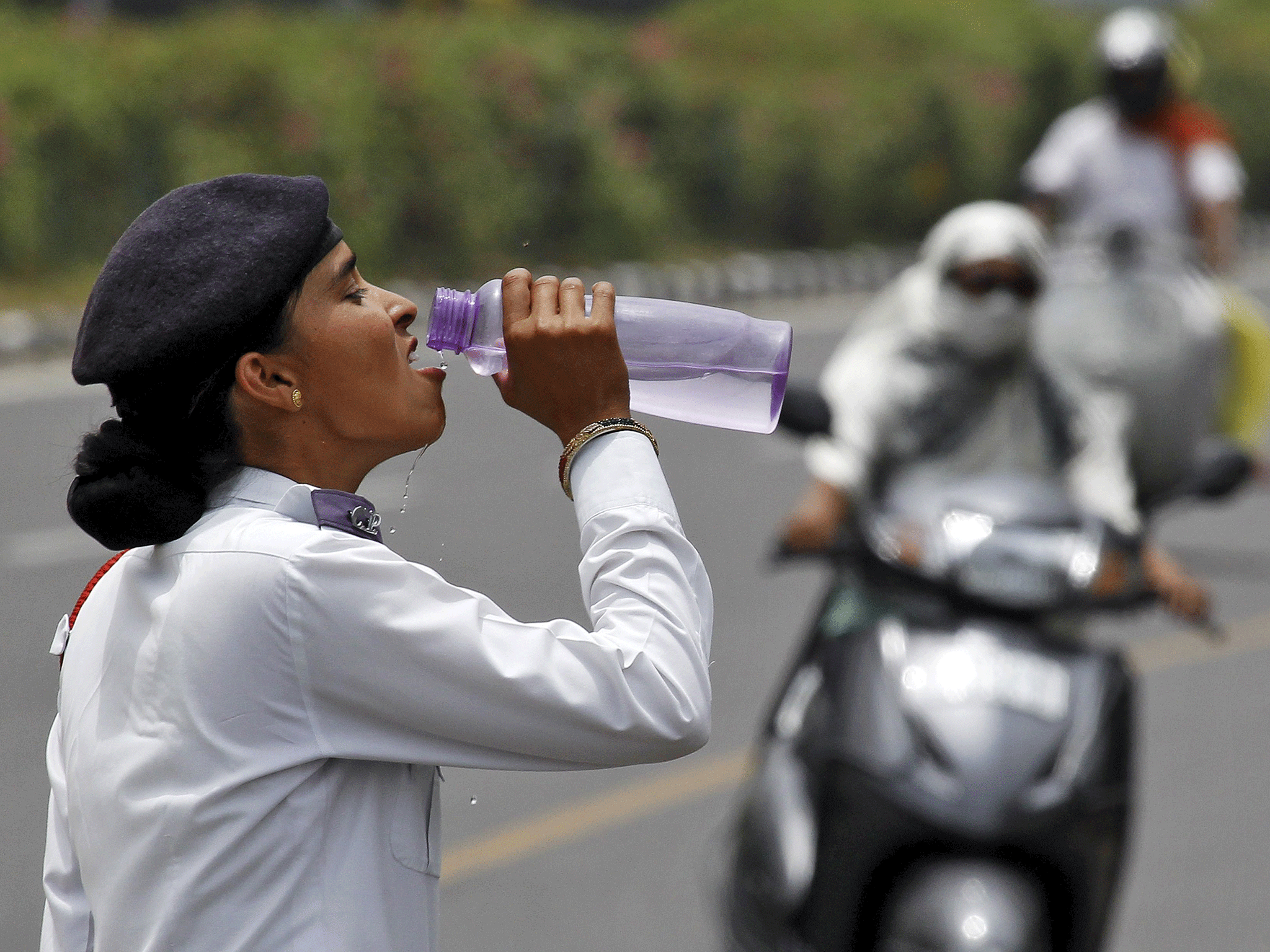 Un agente de policía de tráfico bebe agua mientras los viajeros circulan por una carretera en un caluroso día de verano en Chandigarh en mayo
