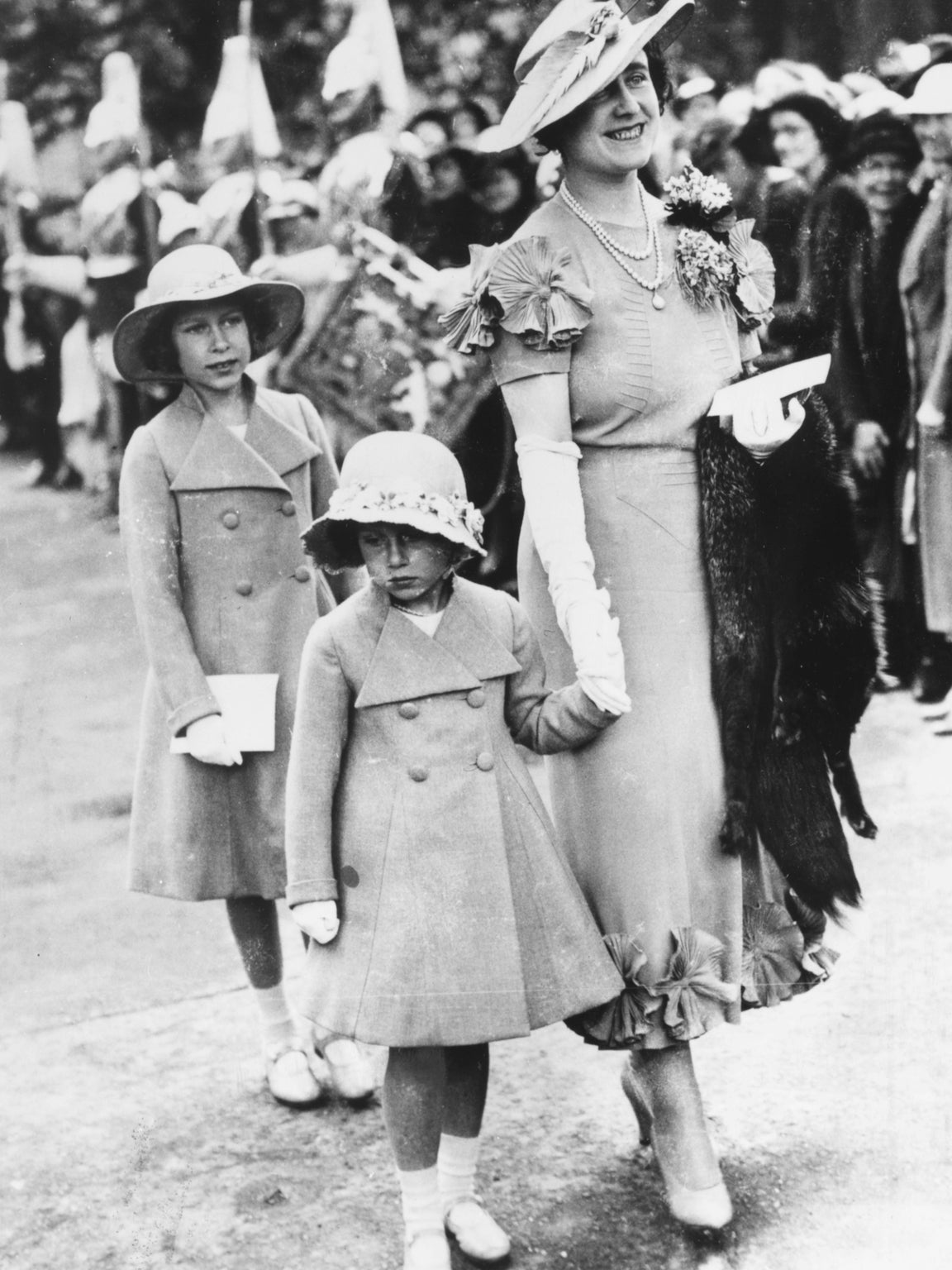 The 9-year-old Elizabeth attends an aristocratic wedding with her mother and younger sister. Later in that year with the death of her Grandfather and the Abdication of her Uncle Edward VIII she became first in line to the throne, 1936