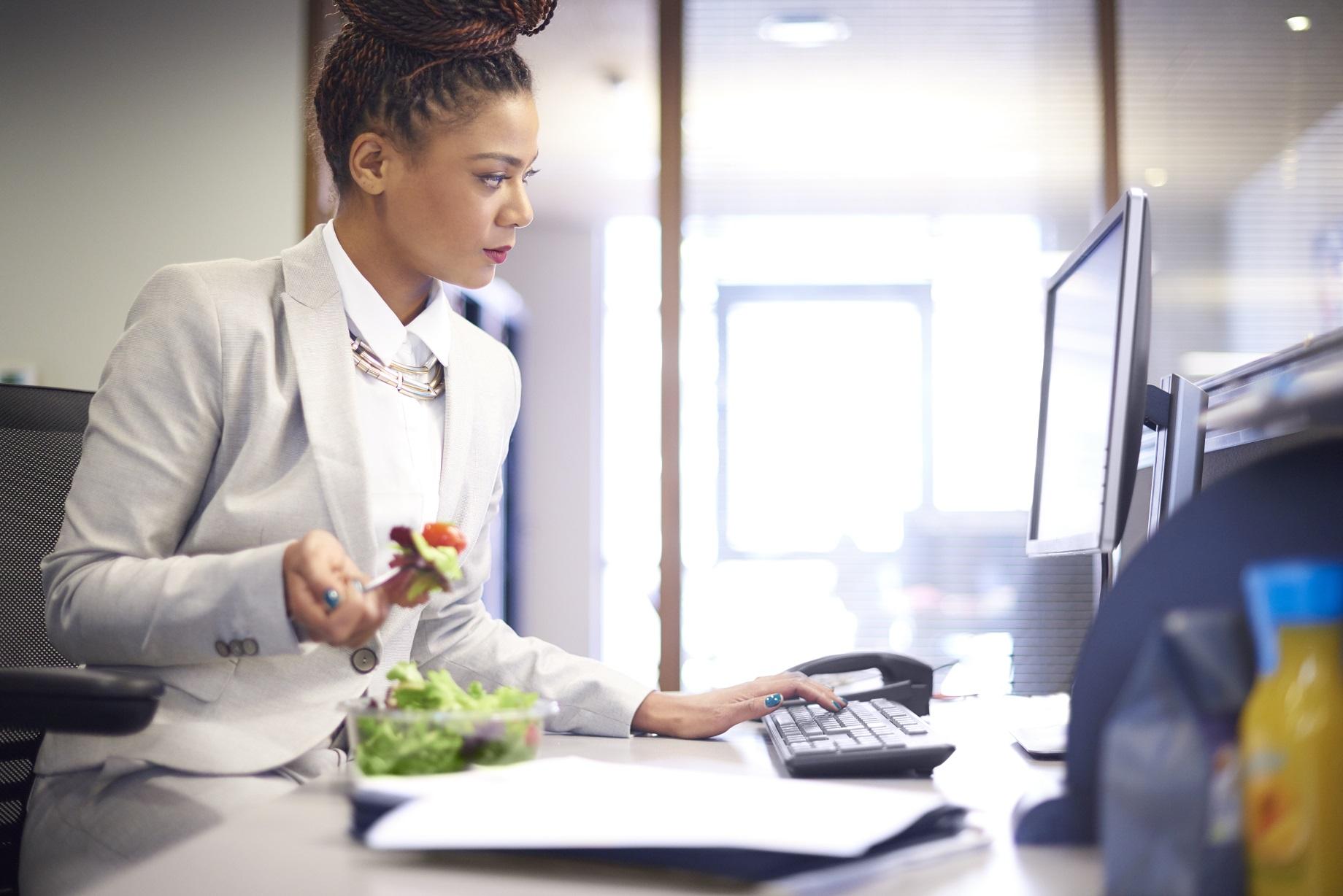Una mujer revisa su computadora mientras come una ensalada