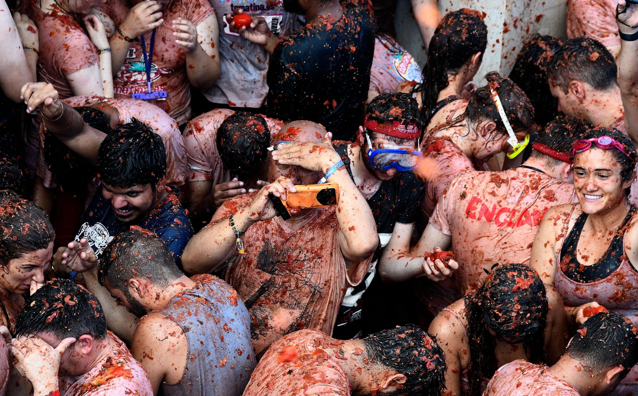 A man takes pictures with a smartphone as revellers throw tomatoes during the 'Tomatina' festival in Bunol, This iconic annual fiesta that takes place on the last Wednesday of August and celebrates its 73rd edition has been billed as "the world's biggest food fight" becoming a major draw for foreigners, in particular from Britain, Japan and the United States.